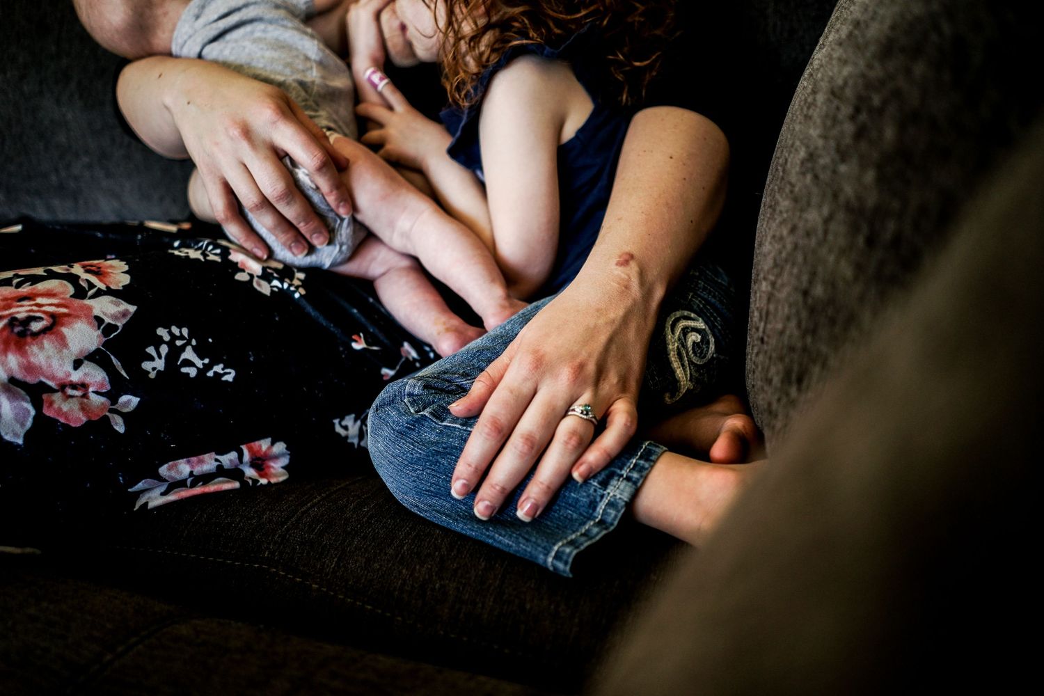 Close-up of two adults hands holding a baby on a floral patterned lap indoors.