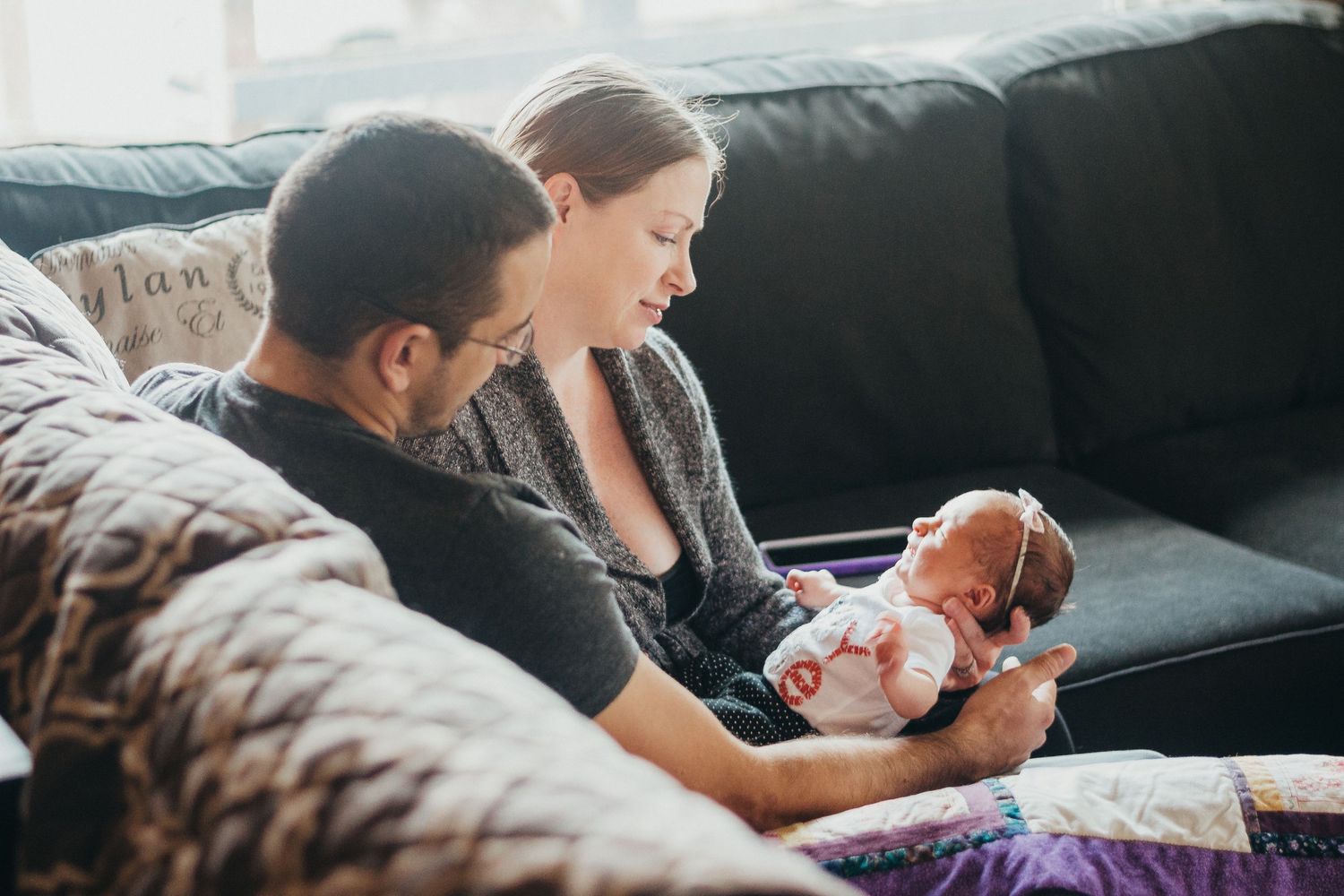 Young couple sitting on a couch together admiring their newborn baby girl.