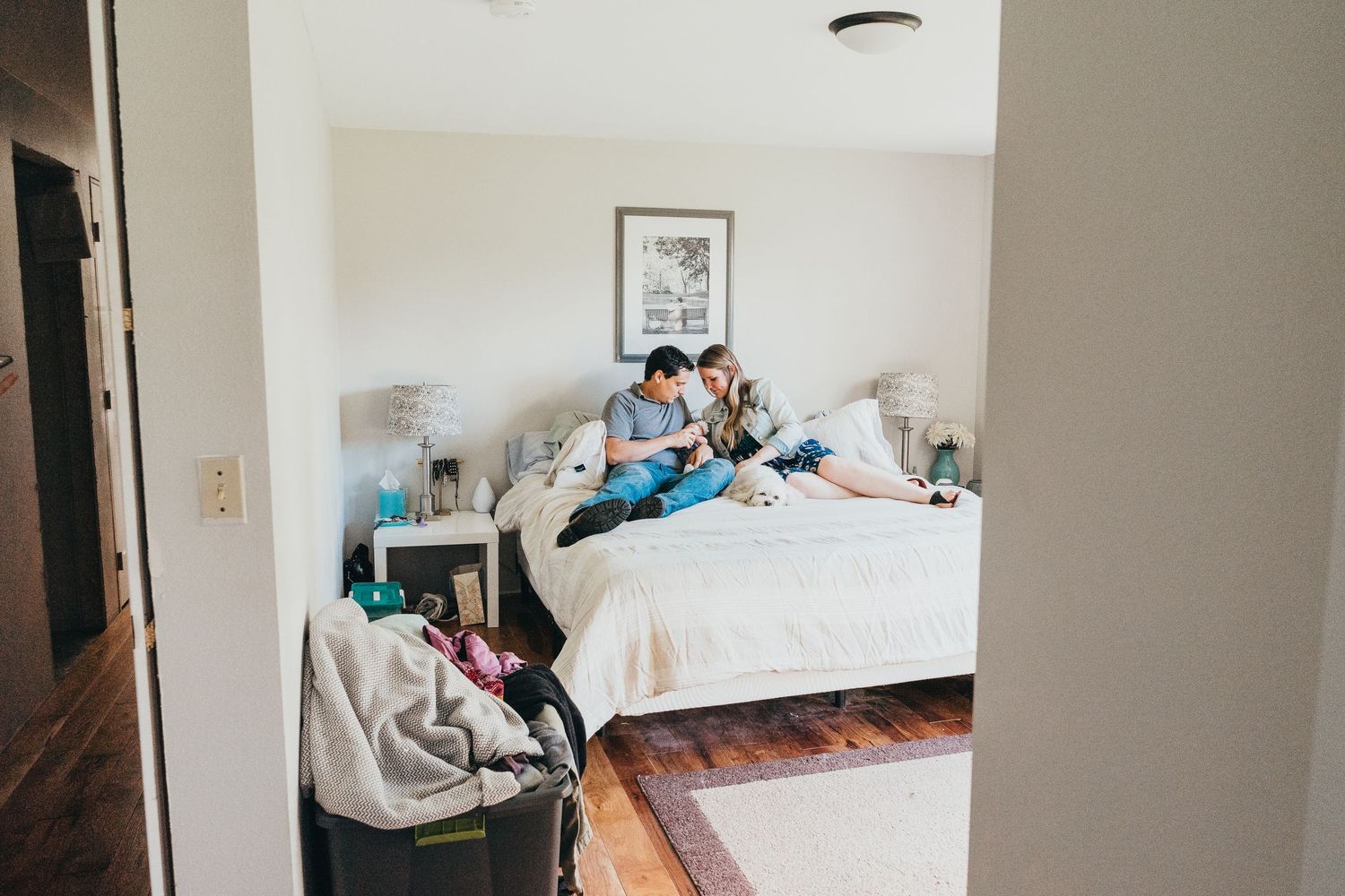 Couple relaxing on bed with newborn baby captured through doorway in lifestyle photo.