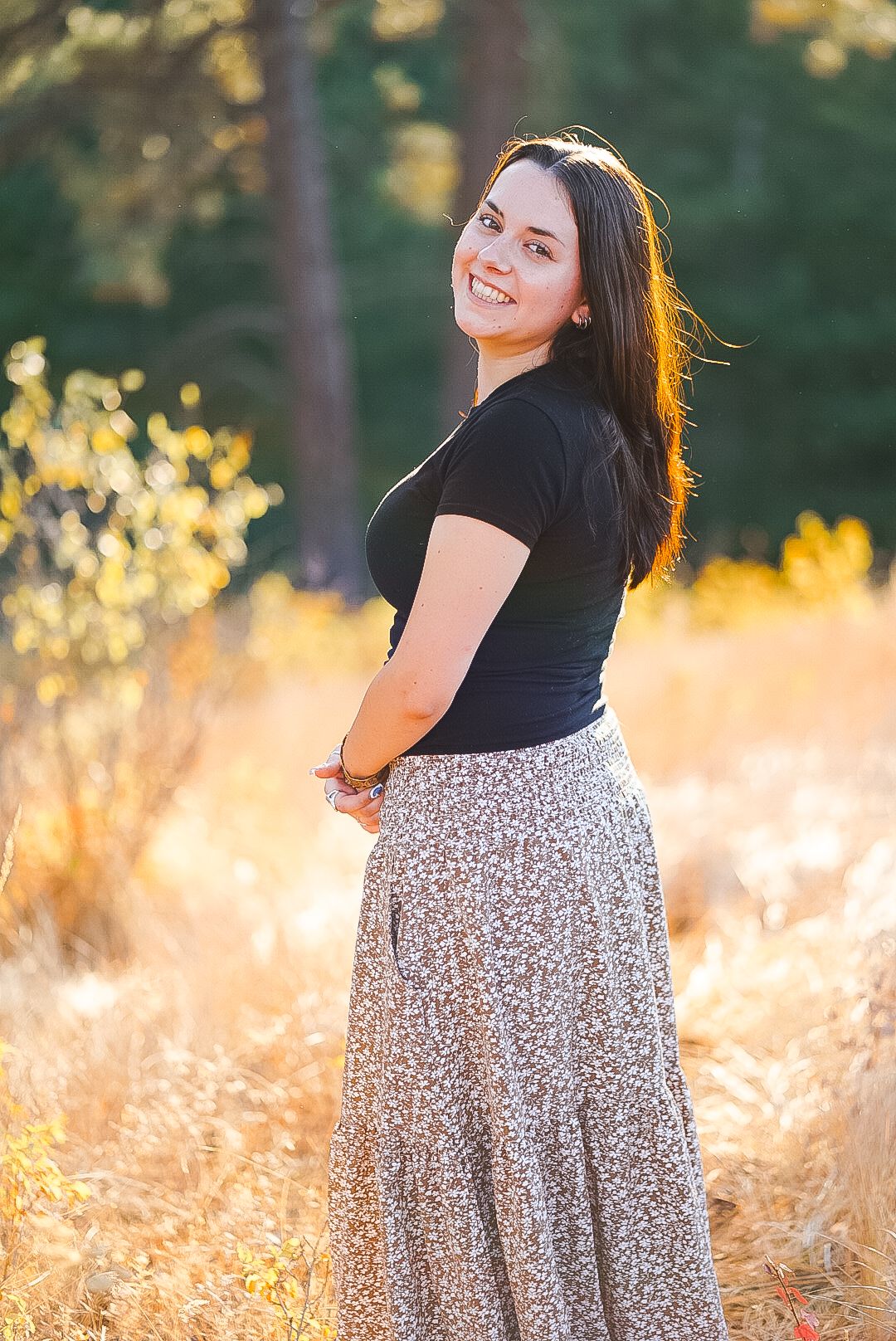 Smiling young woman in black top and floral skirt in golden autumn field.