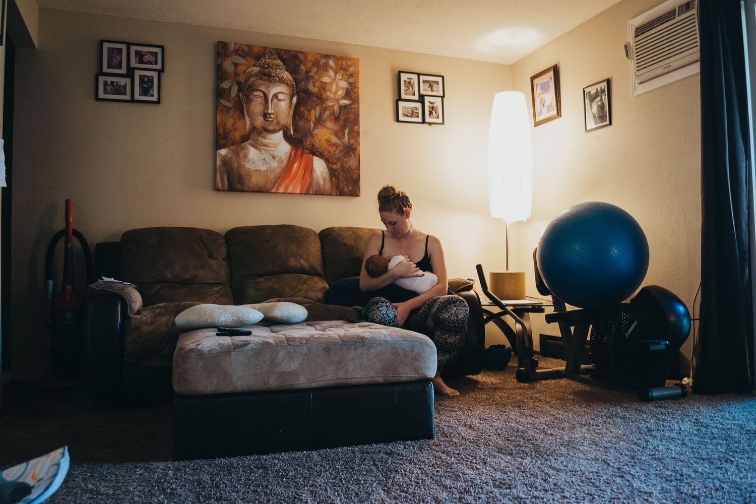 Mother breastfeeding newborn baby on couch in living room with Buddha wall art.