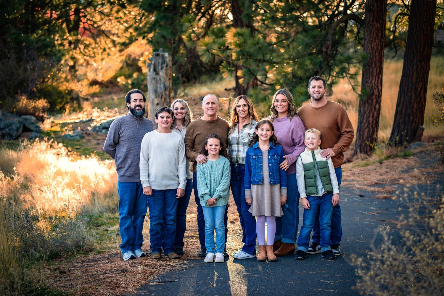 Happy extended family posing together on a tree-lined road at golden hour.