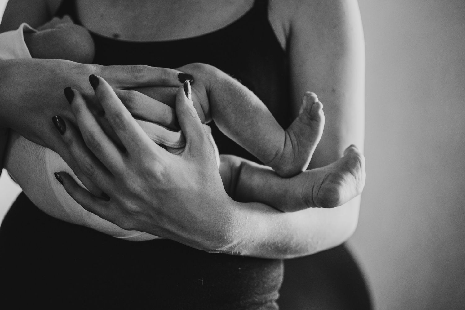 Close-up black and white photo of mother holding newborn baby with tiny feet visible.