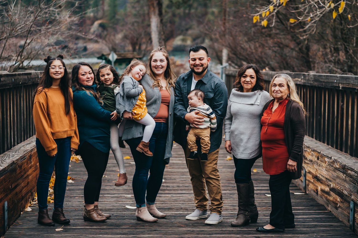 Extended family of eight posing together on a wooden bridge during autumn season.