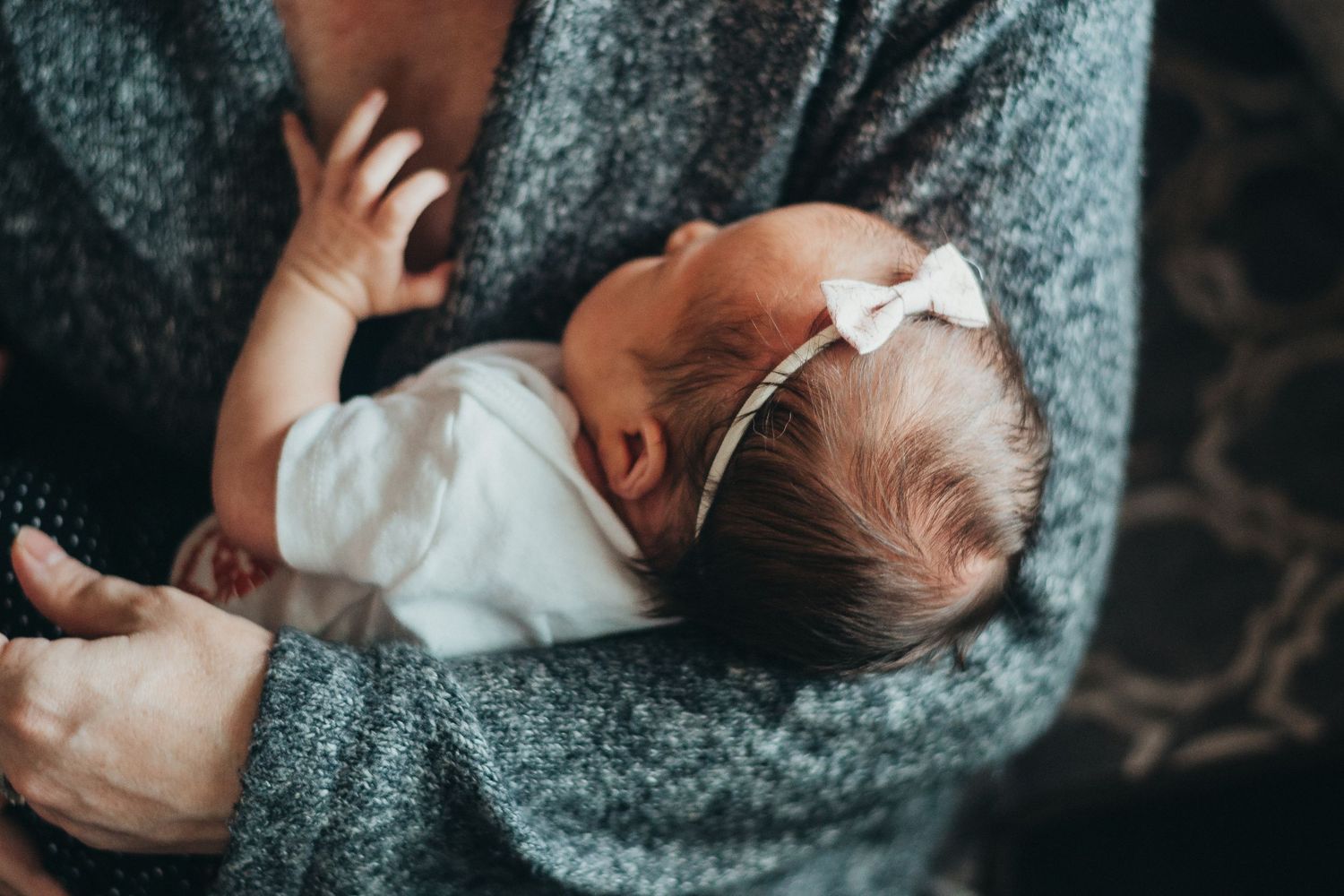 Mother cradling her newborn baby girl wearing a white bow headband in her arms.