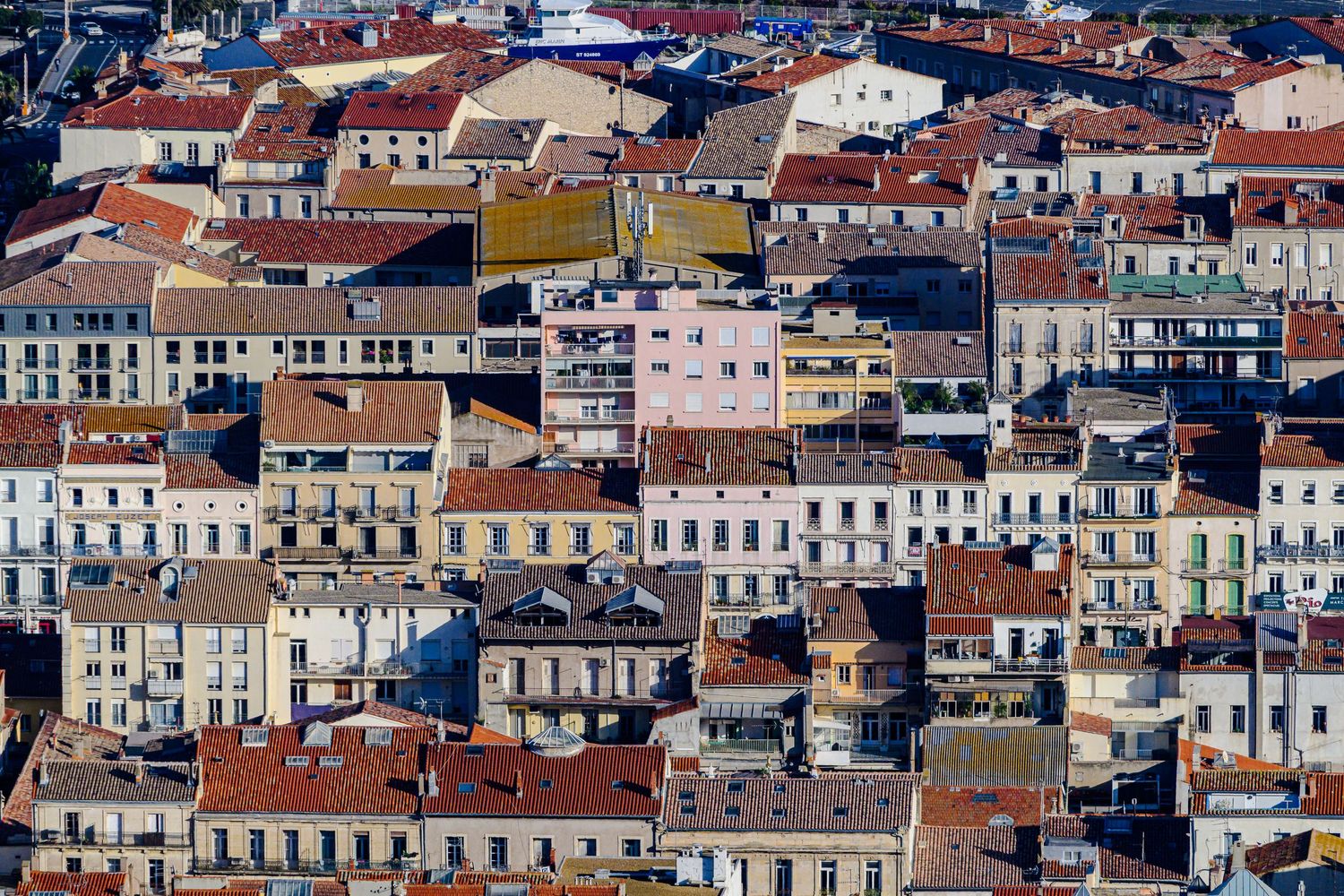 Aerial view of densely packed colorful European buildings with terracotta rooftops in a Mediterranean city.