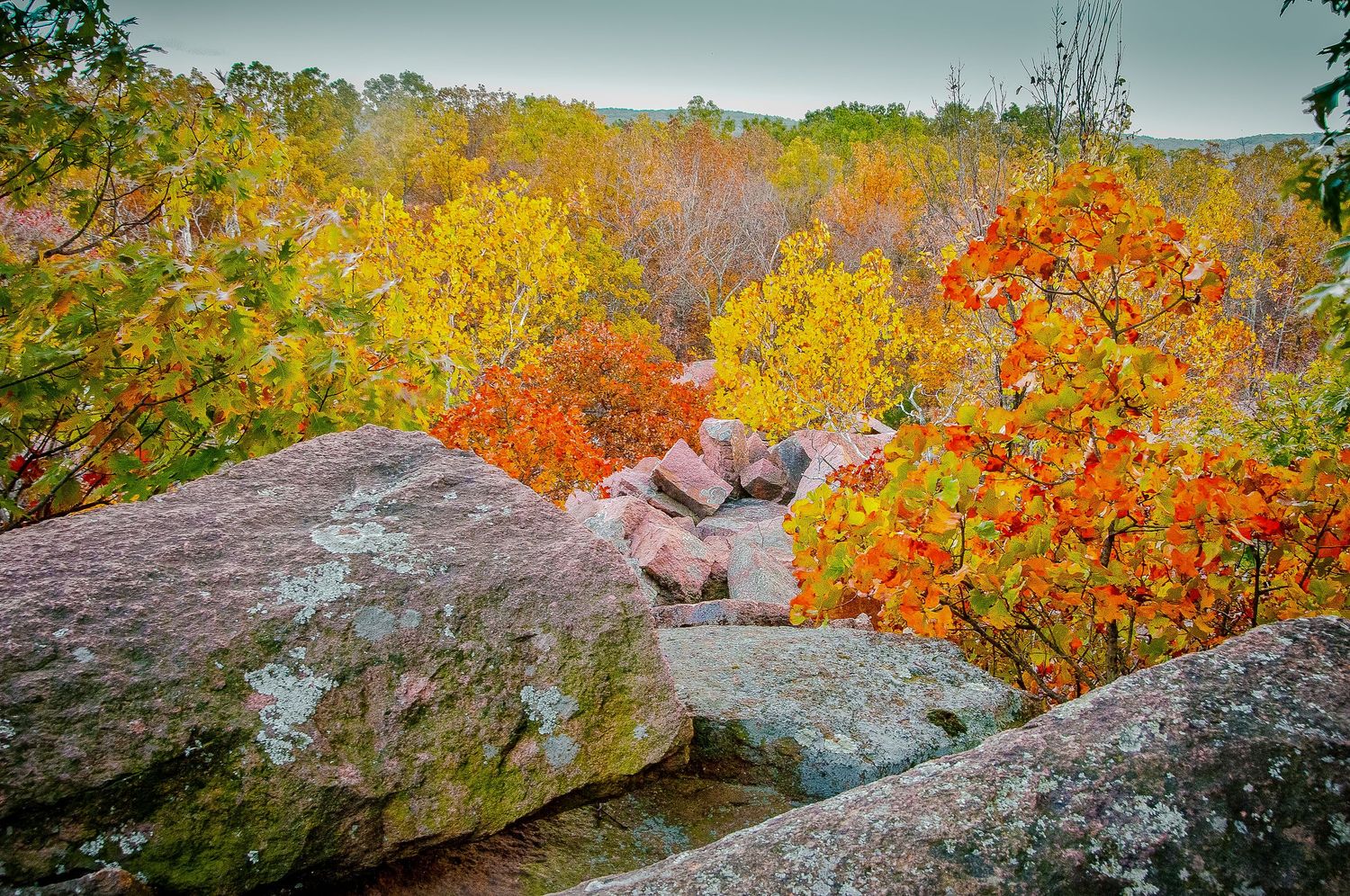 Vibrant autumn foliage in red, orange, and yellow surrounds large granite boulders on a rocky overlook.