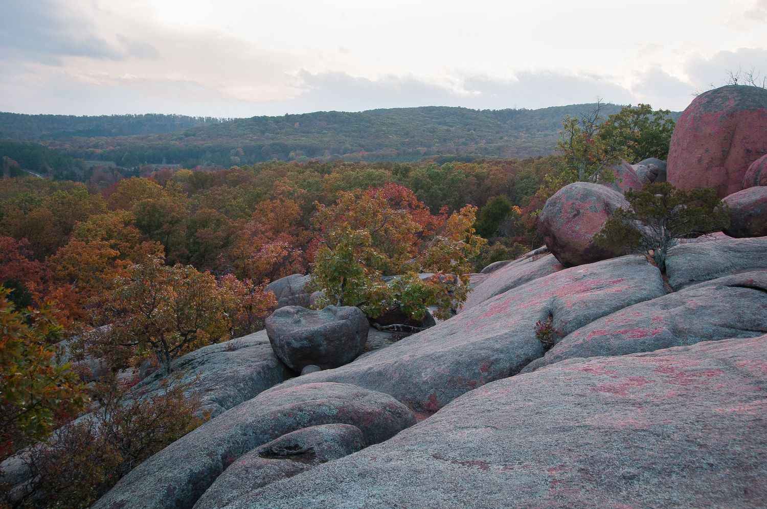 View from granite rock outcroppings overlooking a forested valley with colorful autumn foliage under overcast skies.