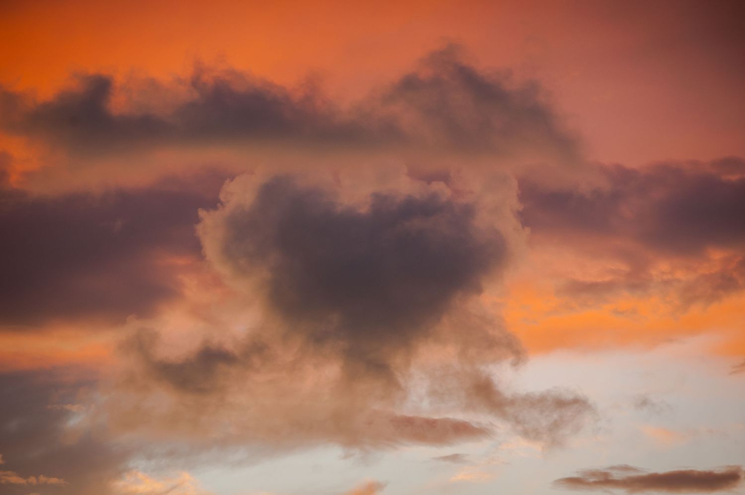 Heart-shaped dark cloud formation against a vivid orange and purple sunset sky.