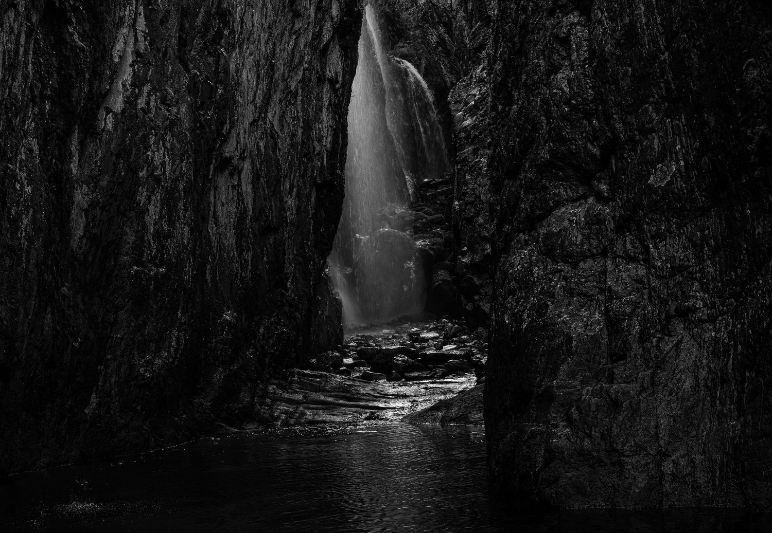 A dramatic black and white photo of a waterfall inside a dark rocky cave.