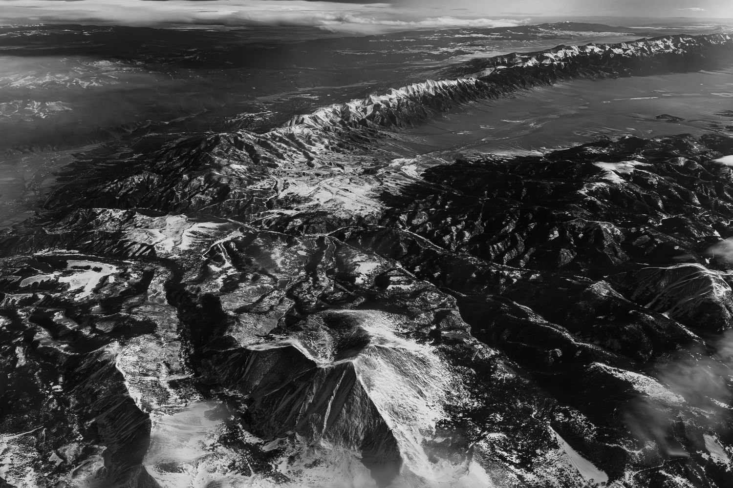 Aerial black and white panoramic view of snow-dusted mountain ranges stretching across a vast landscape.