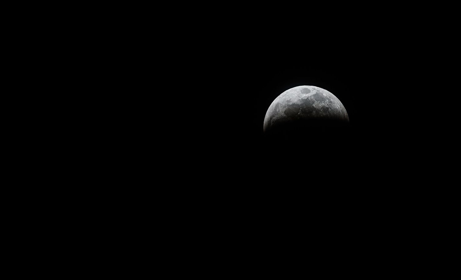 A partial lunar eclipse shows the moon half in shadow against a dark night sky.