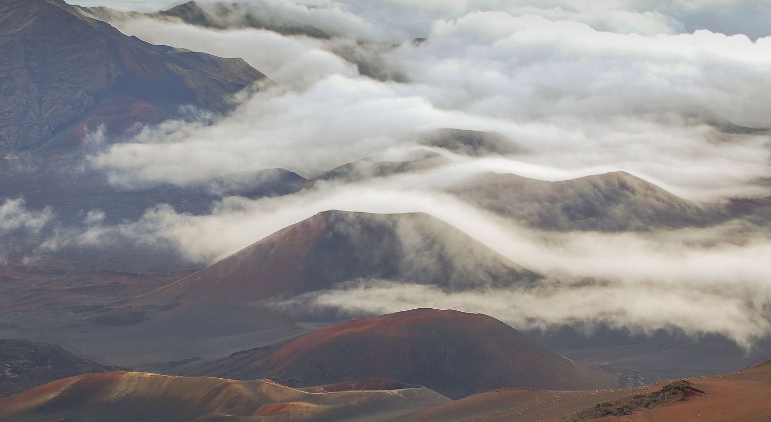 Aerial view of volcanic mountain peaks with dramatic cloud formations rolling through Haleakala crater in Maui, Hawaii.