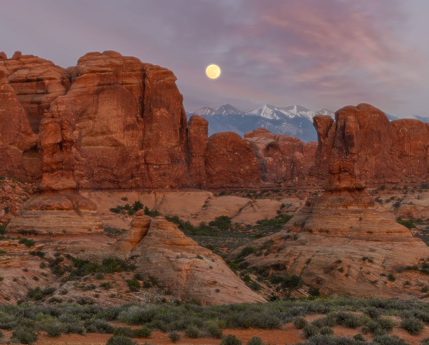 Full moon rising over red rock formations at Arches National Park at sunset.