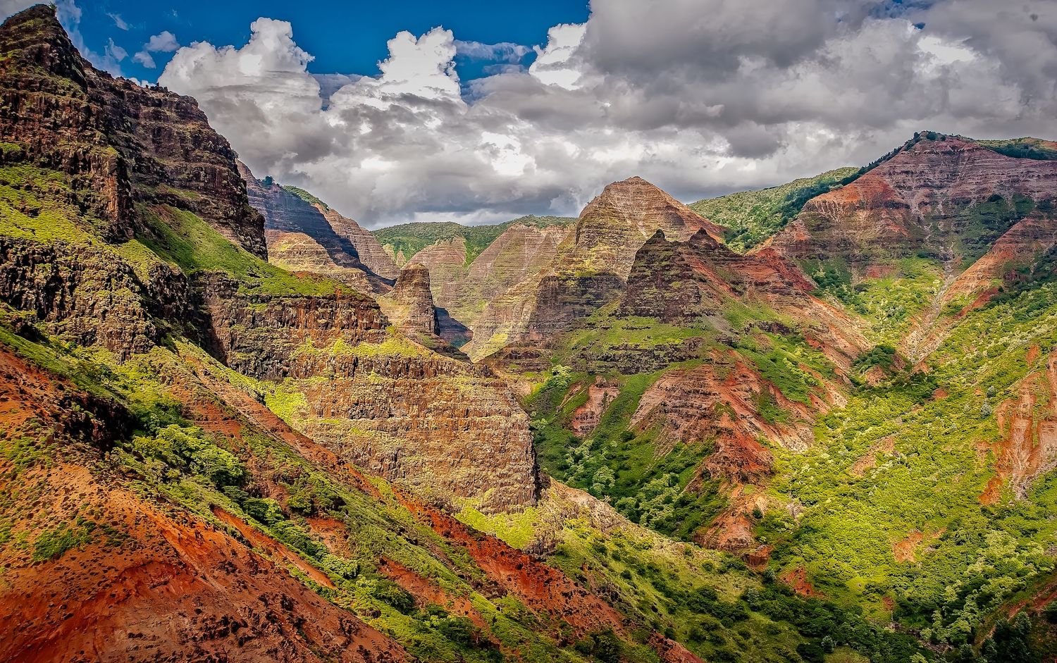 Vibrant red and green layered mountain valleys of Waimea Canyon under dramatic clouds in Kauai Hawaii.