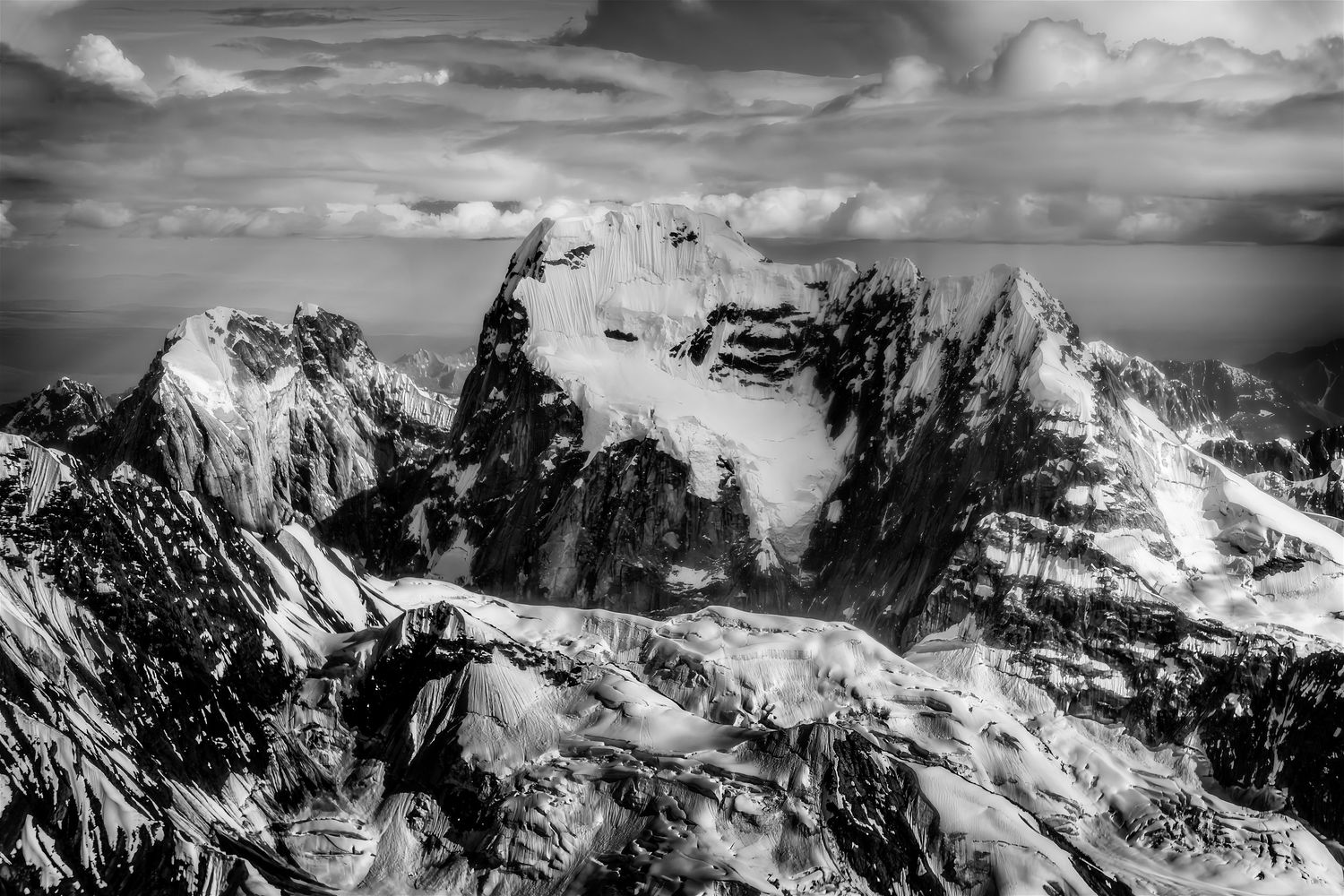 Dramatic black and white aerial view of snow-covered rocky mountain peaks with glaciers.