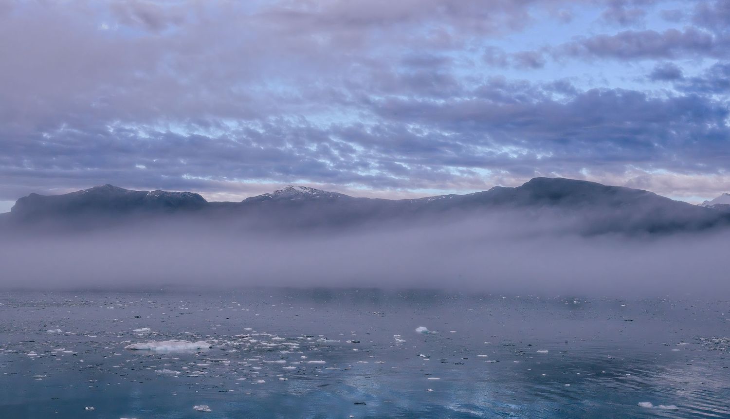 Misty Arctic waters with floating ice and fog-covered mountains at dusk.