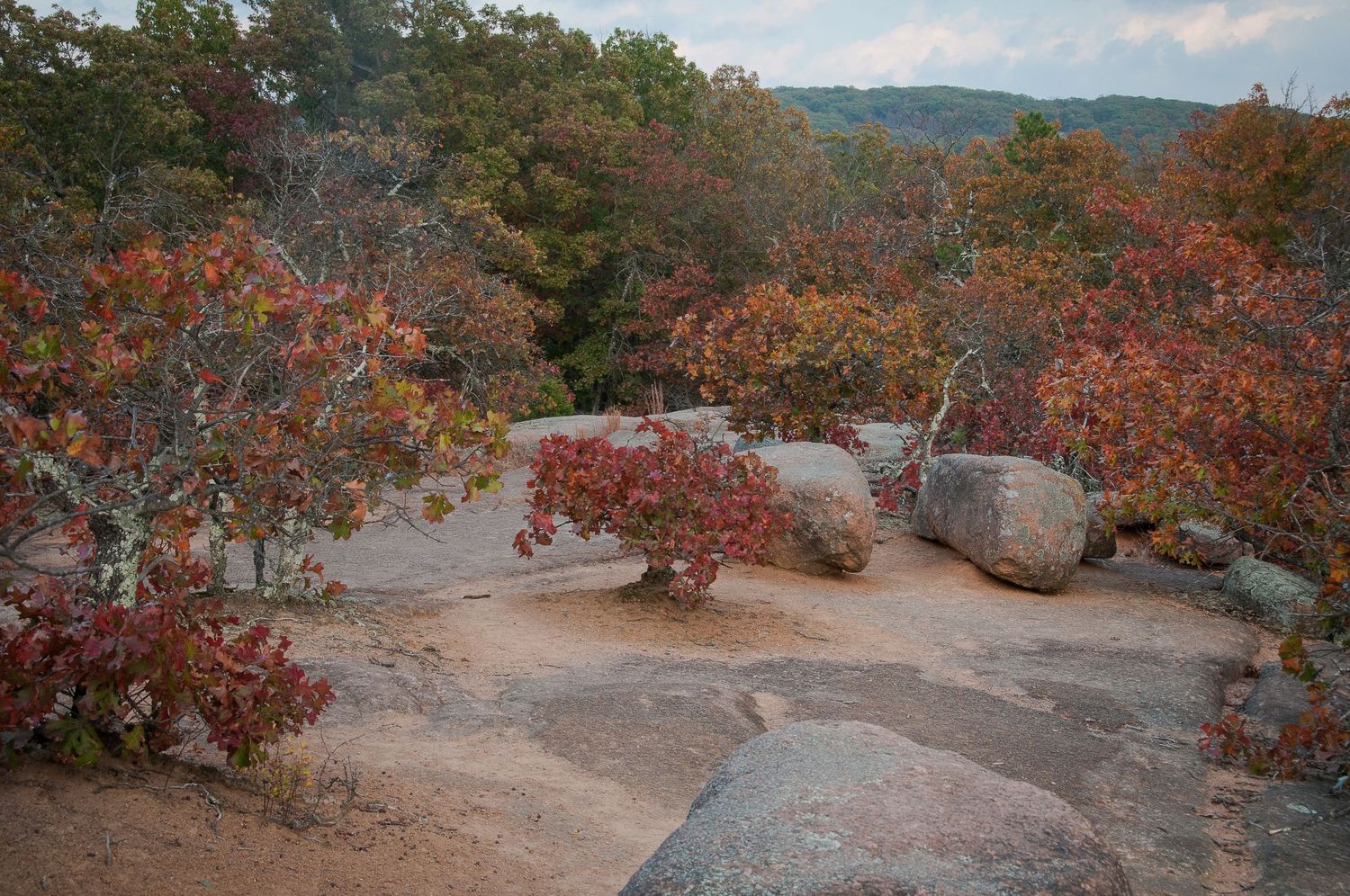 Autumn foliage with red and orange trees among granite boulders on a rocky overlook in a forested landscape.