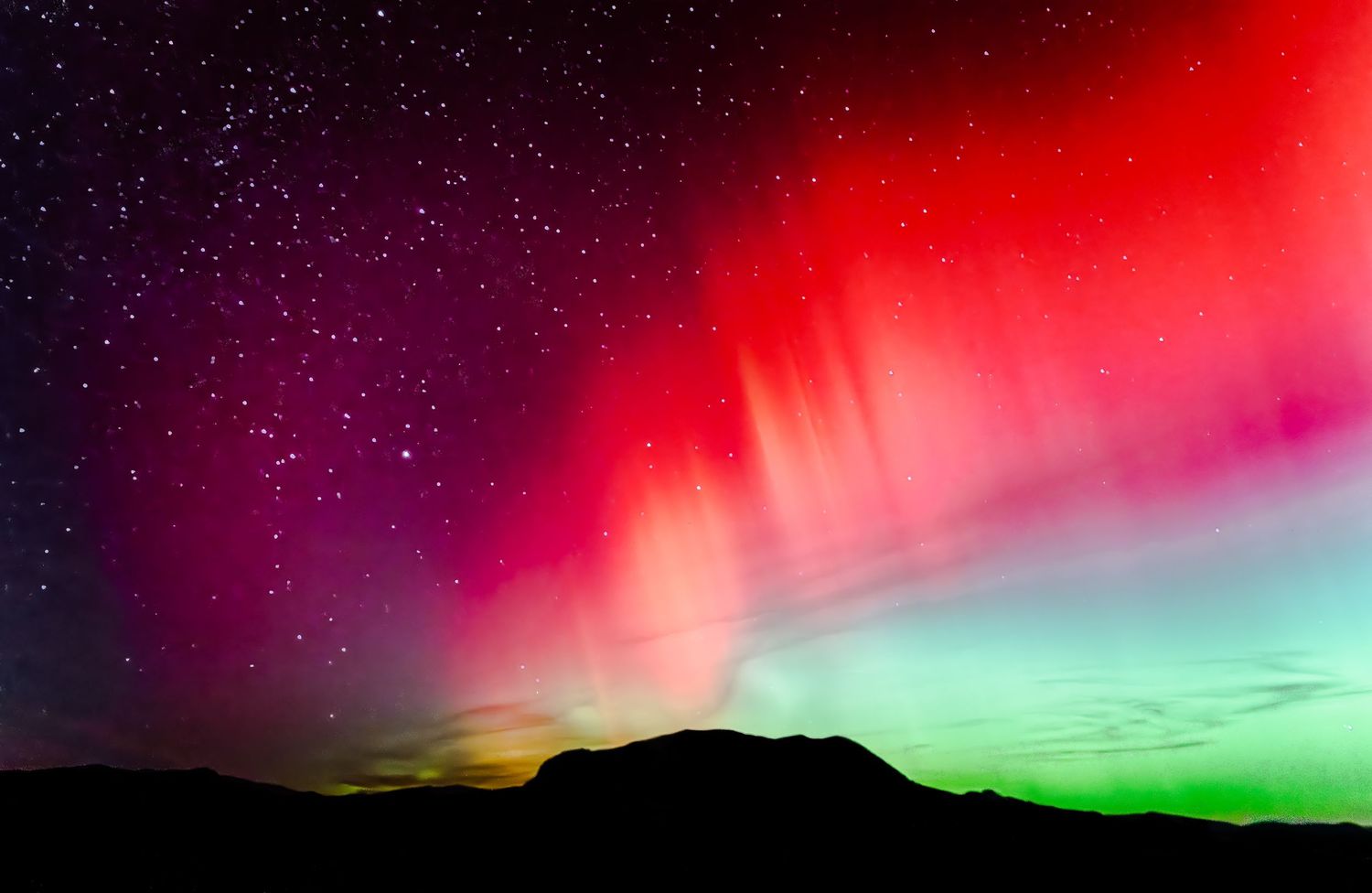Stunning aurora borealis northern lights display red green and purple colors over a dark mountain silhouette.
