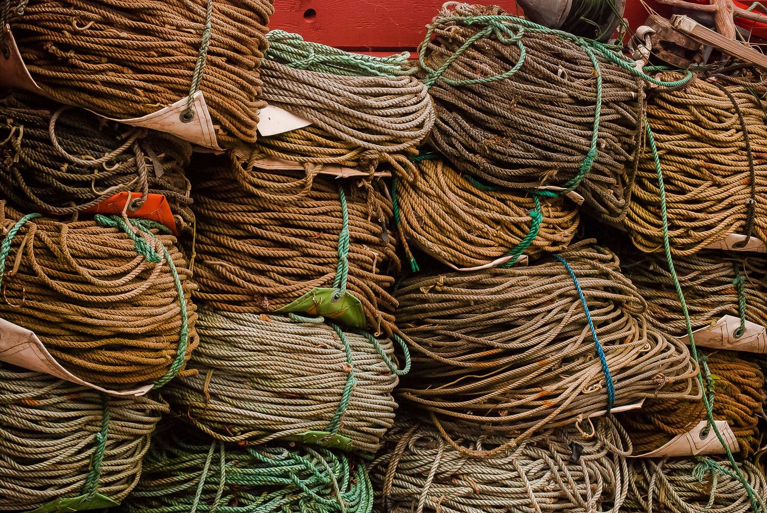 Large bundles of coiled golden and green fishing ropes stacked in a pile at a harbor.