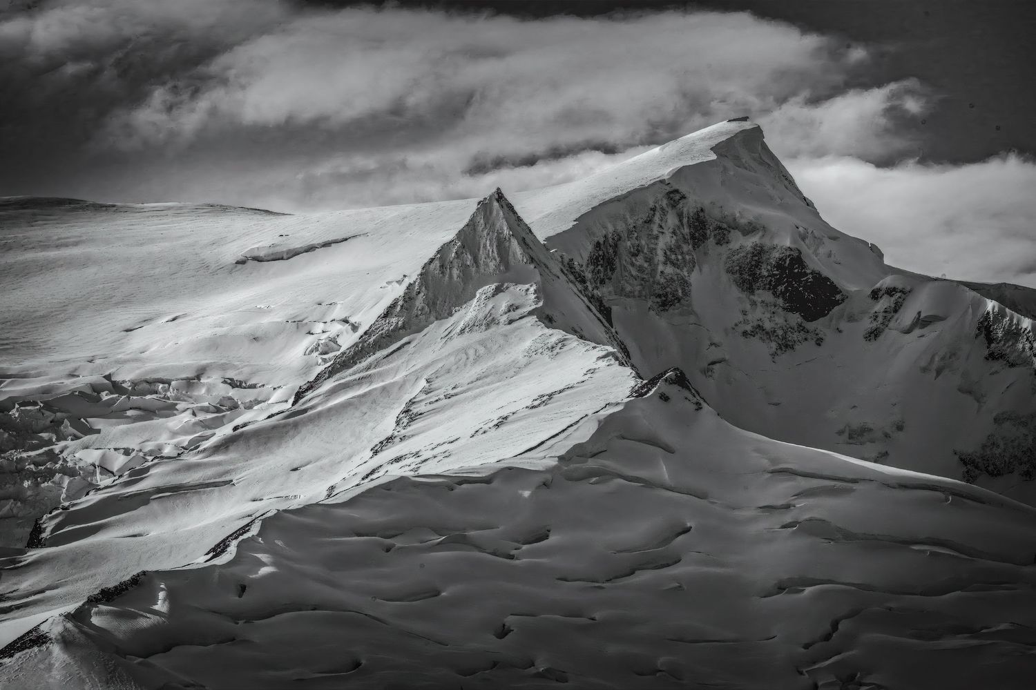 Black and white dramatic snow-covered mountain peaks rise sharply under a cloudy alpine sky.