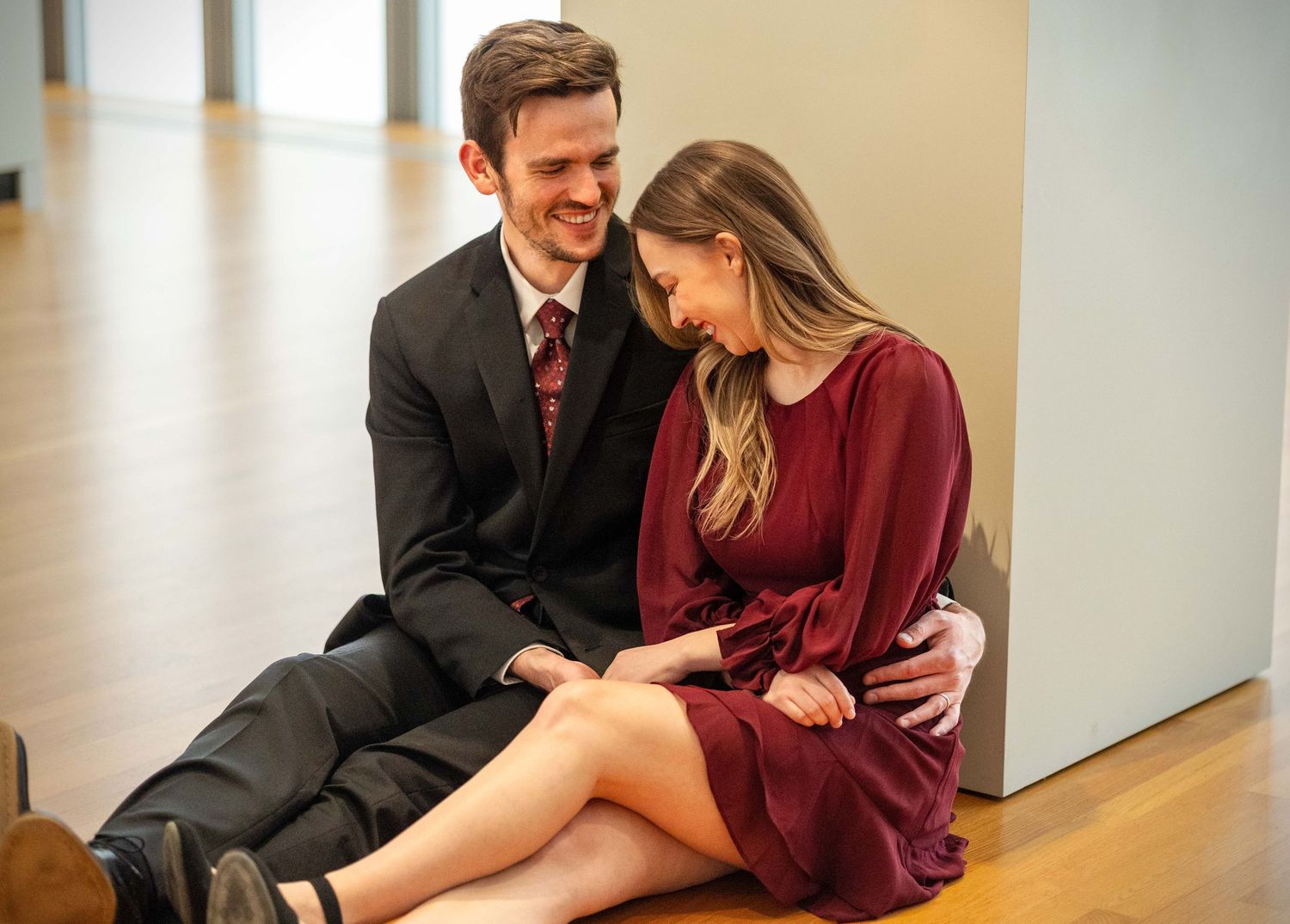 Young couple sitting on a floor, smiling and sharing an intimate moment indoors.