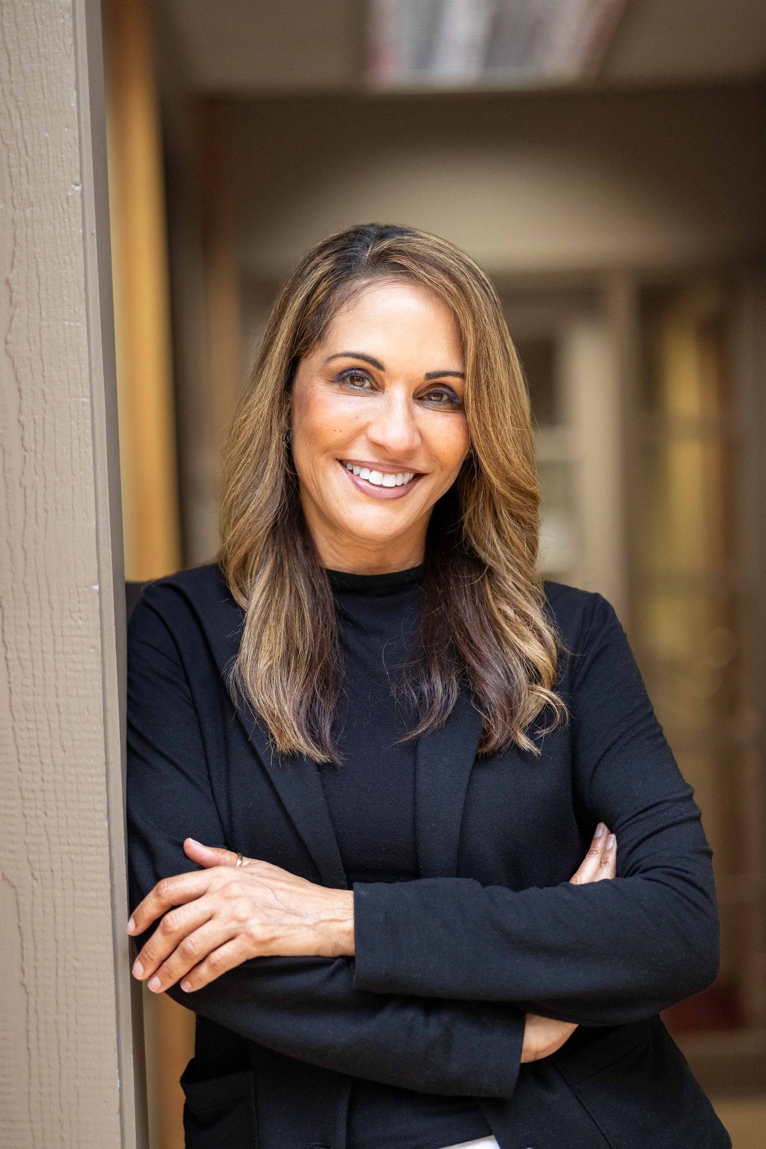 Confident woman in black blazer with arms crossed smiling outdoors.
