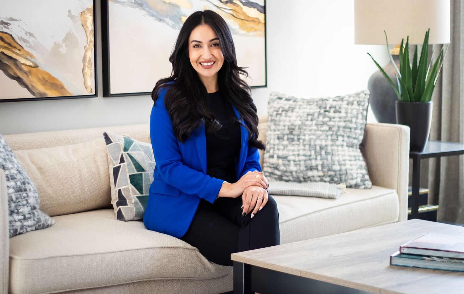 Professional woman in blue blazer sitting confidently on a modern sofa in a stylish interior.