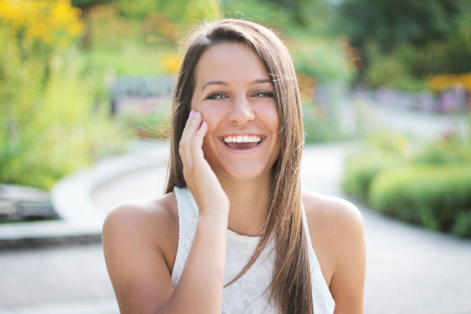 Beautiful young woman smiling warmly in sunny garden with hand resting on her cheek.
