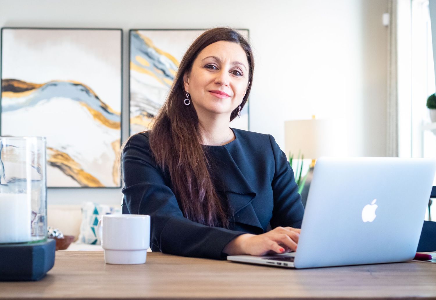 Professional woman smiling while working on Apple laptop at modern home office desk.