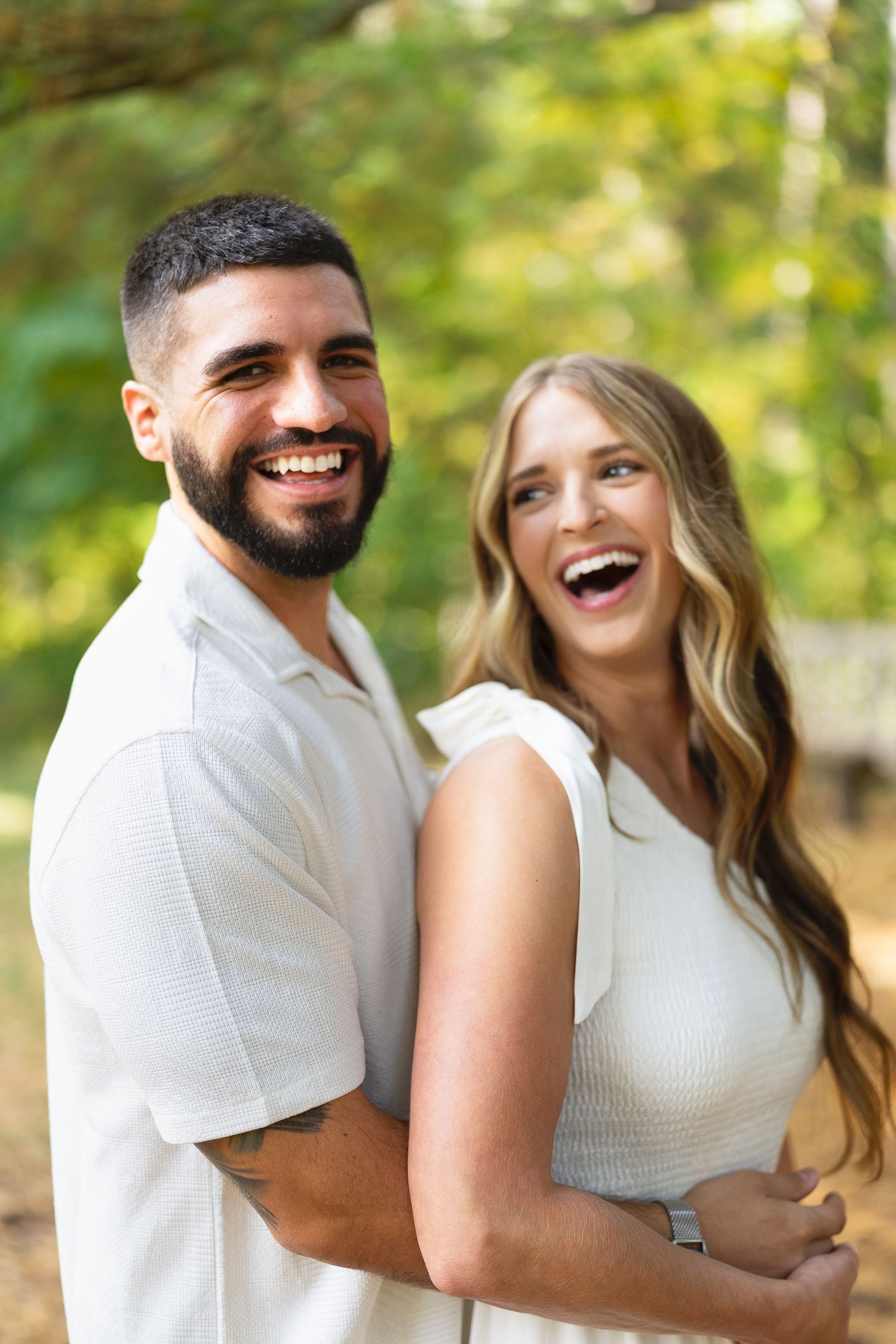 Happy smiling couple laughing outdoors in green park setting, man with beard in white polo shirt.