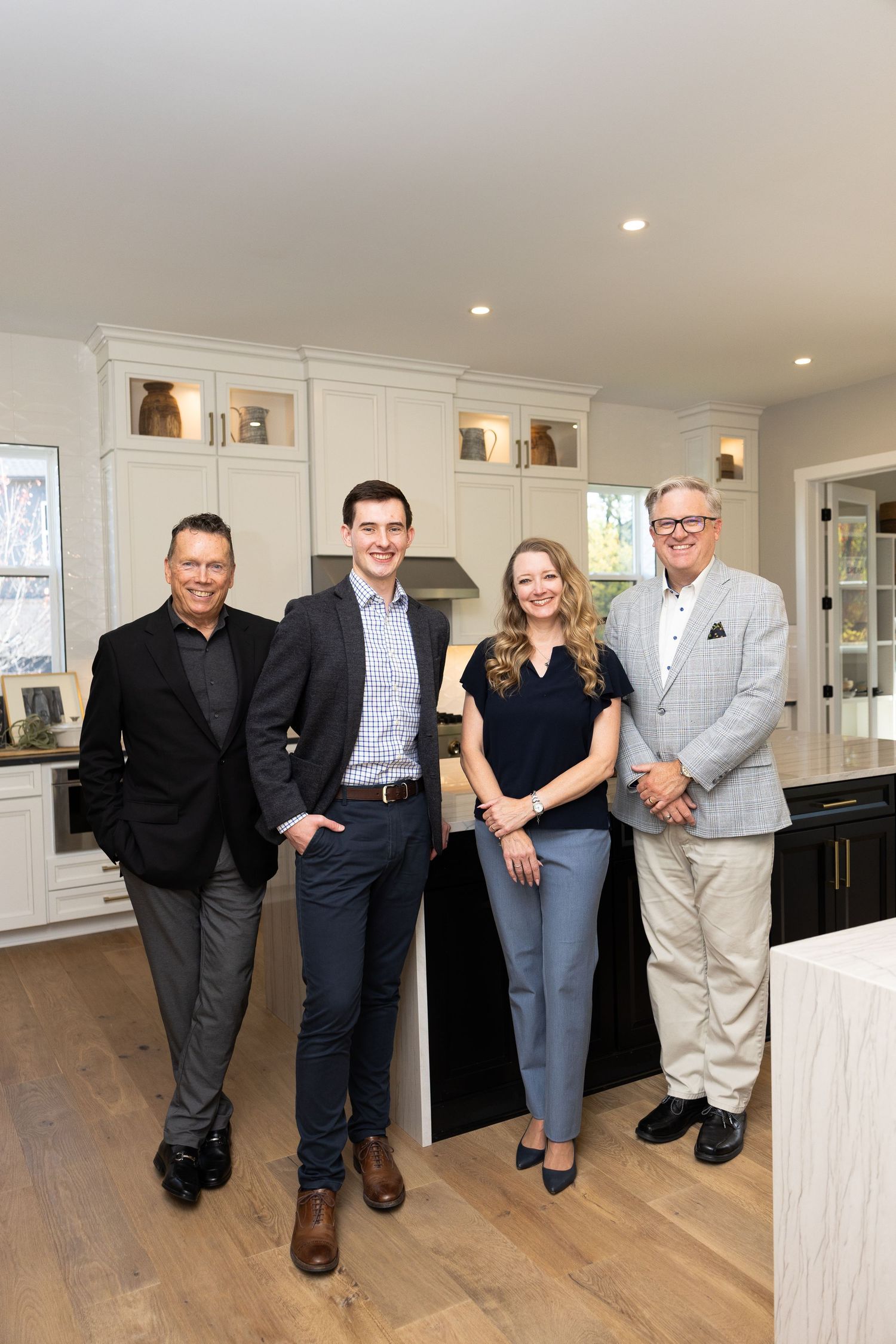 Four real estate professionals smiling together in a modern white kitchen with hardwood floors.