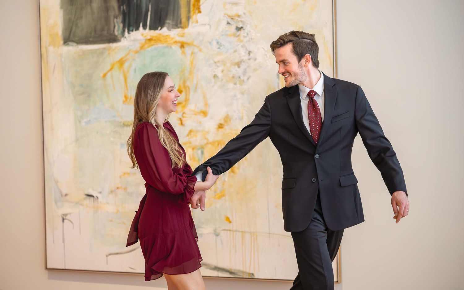 Couple holding hands and smiling in front of abstract art painting in a gallery.
