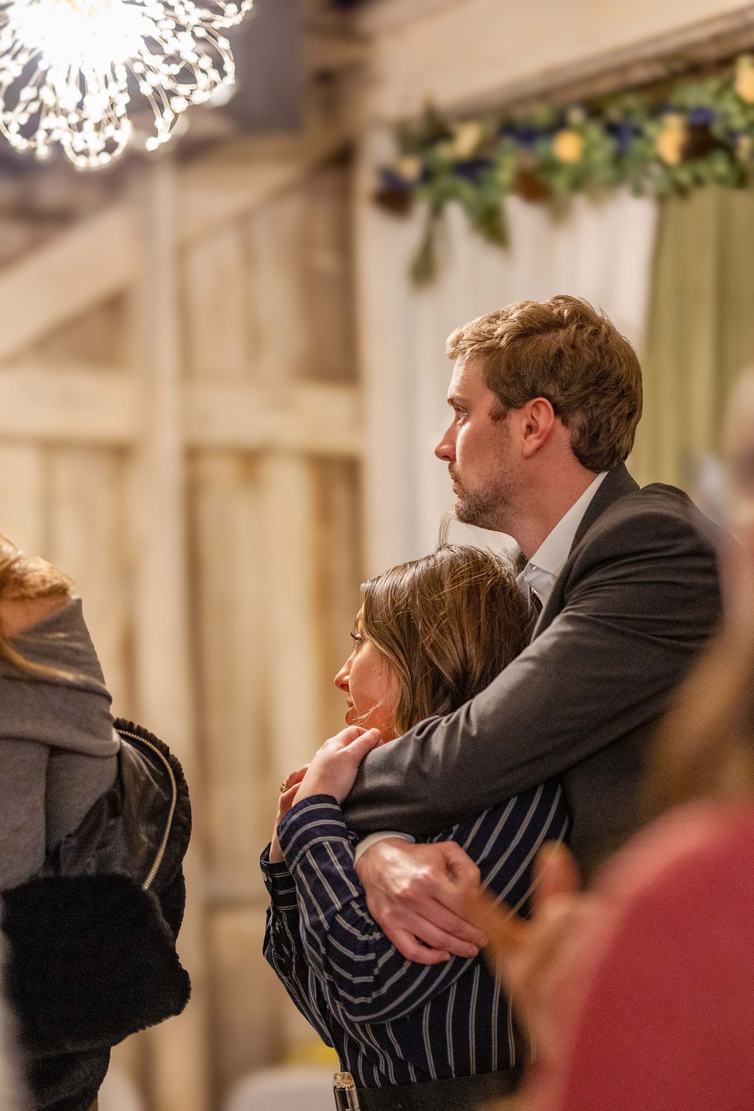 A man tenderly embraces a woman at a warmly decorated indoor wedding venue with festive lighting.