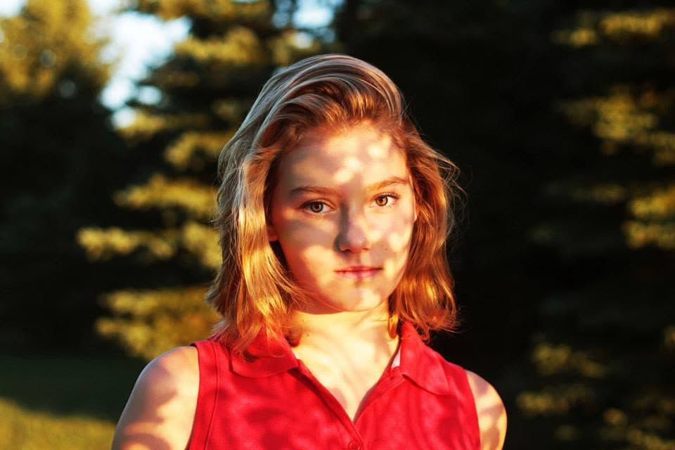 Young girl with short auburn hair in red sleeveless top outdoors in golden evening light.