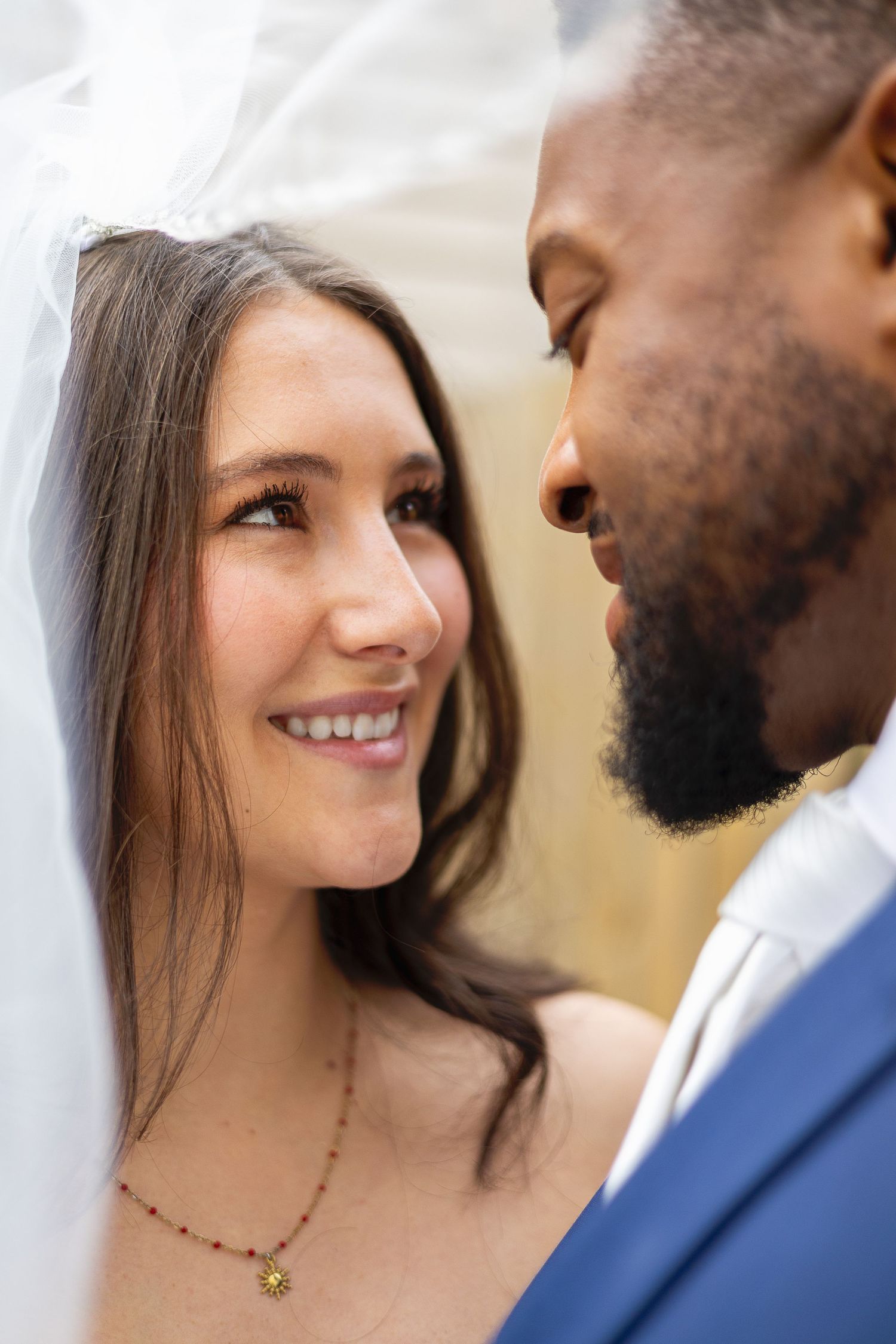 A smiling bride in a veil gazes lovingly at her bearded groom during their wedding.