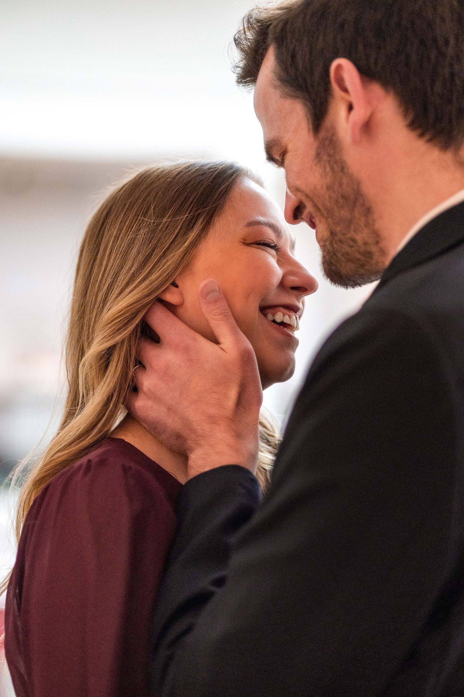 A smiling couple shares a tender romantic moment, the man gently cupping the womans face as they lean in close.