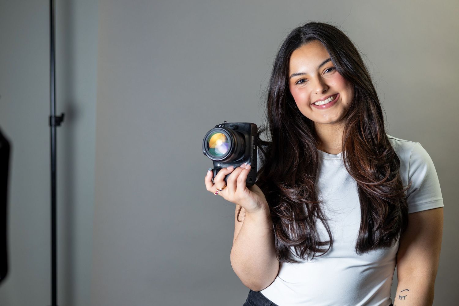 Smiling female photographer holding a DSLR camera in a professional studio setting.