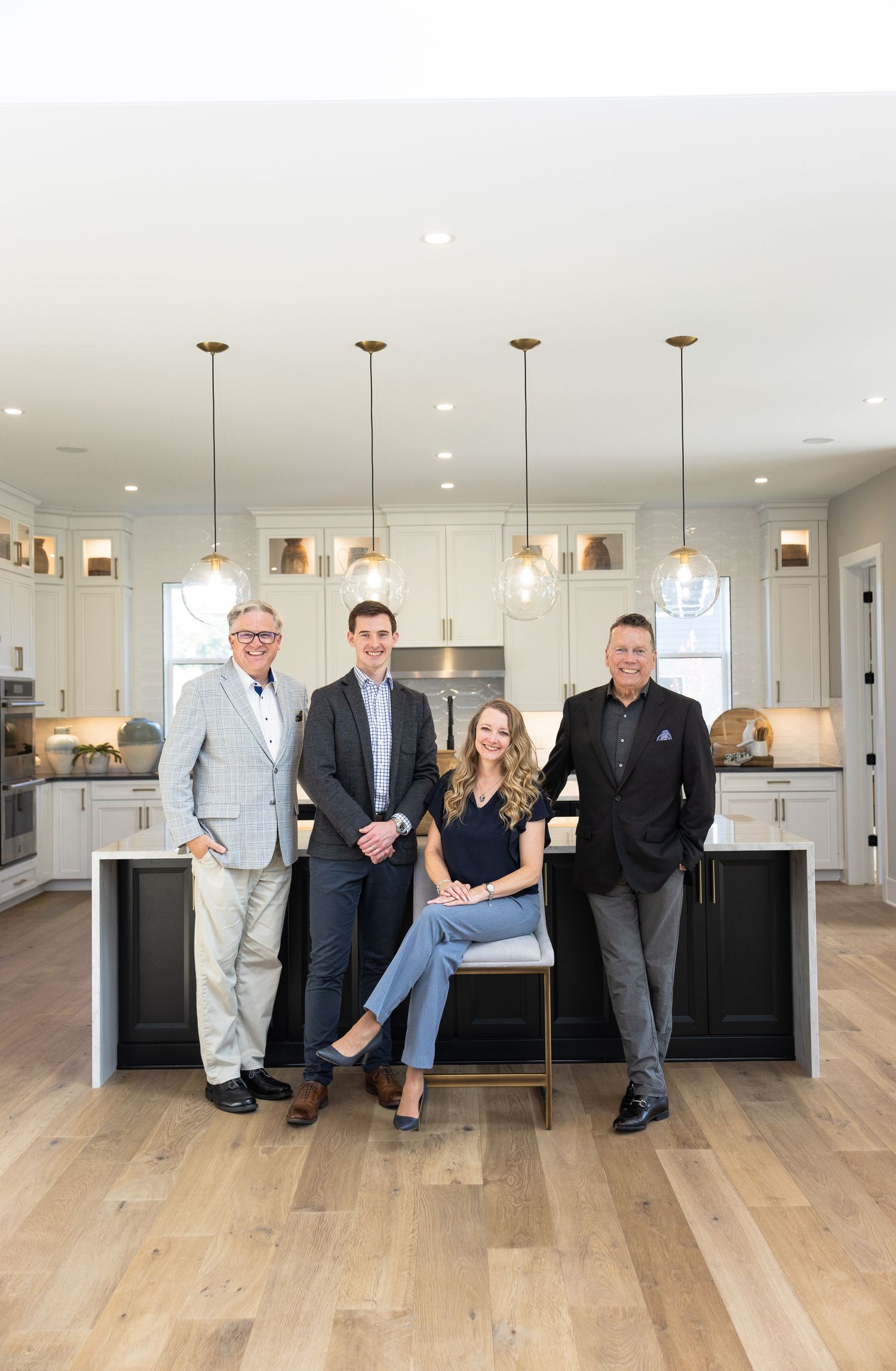 Four real estate professionals posing together in a modern white kitchen with hardwood floors and pendant lights.