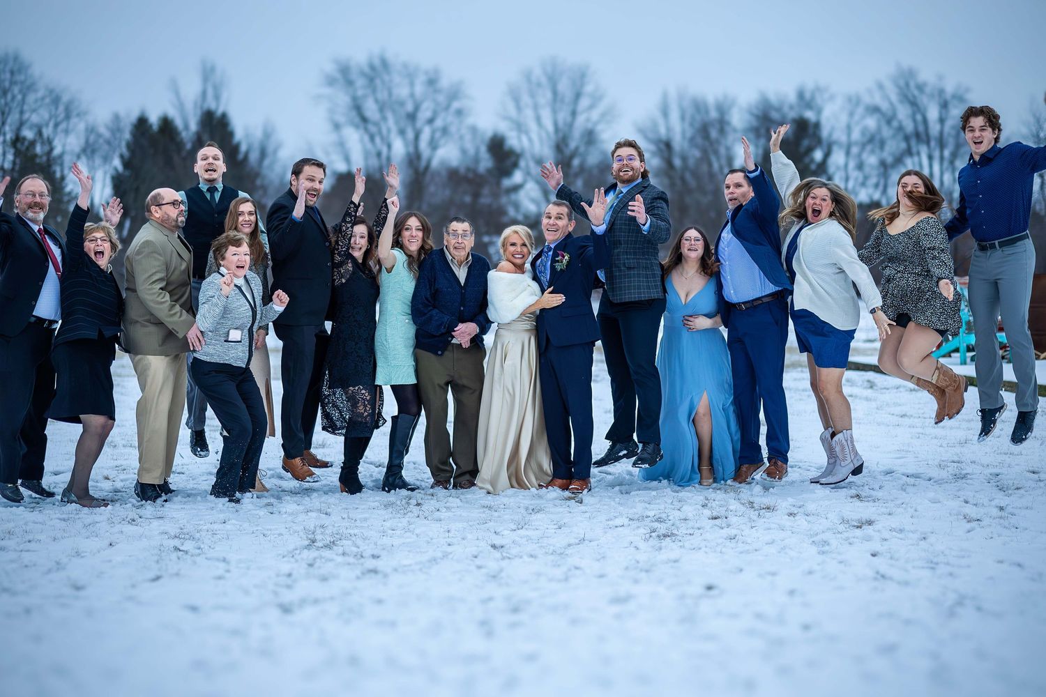 Wedding party celebrating outdoors in winter snow, jumping joyfully in formal and semi-formal attire.