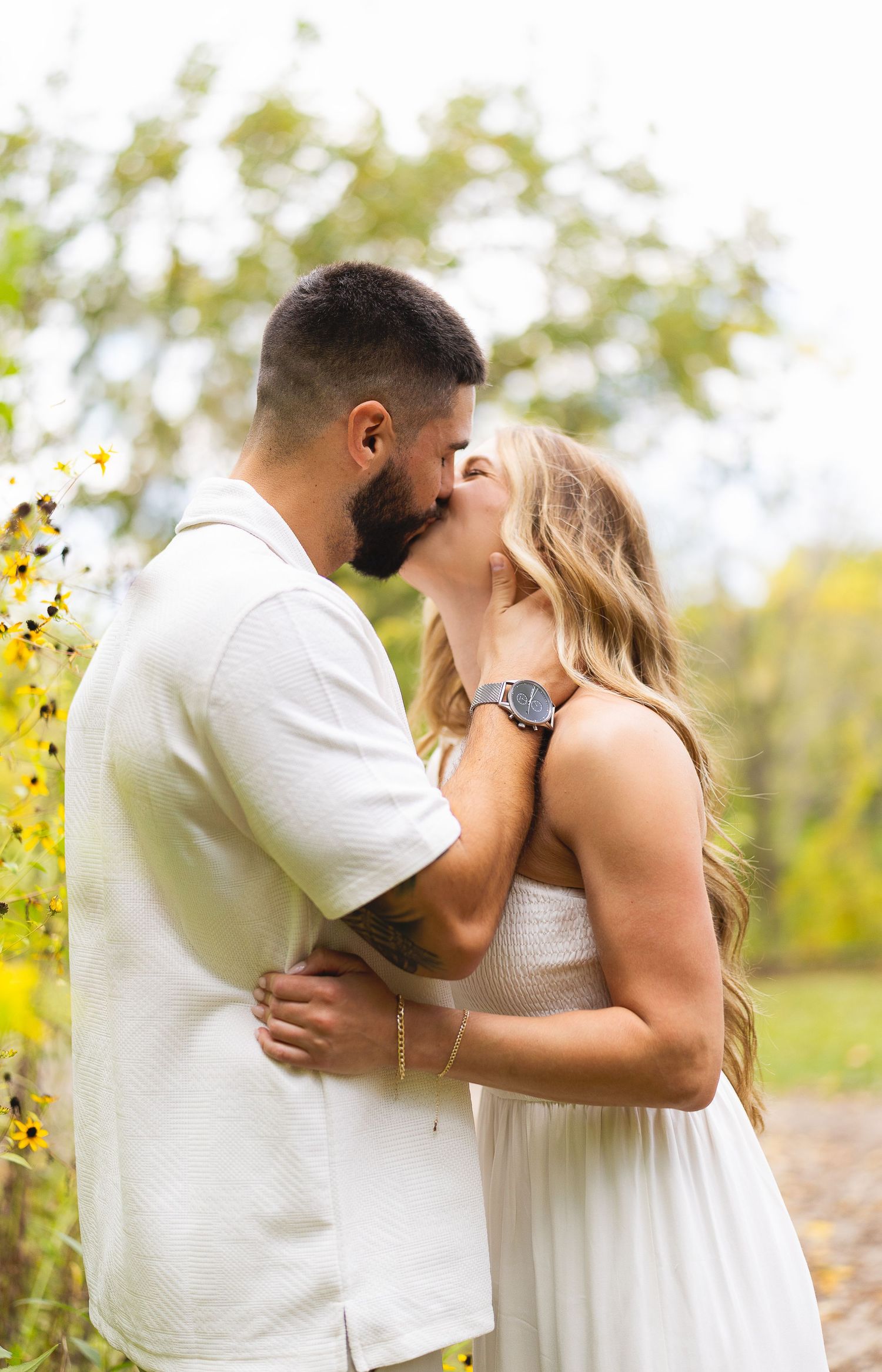 A couple shares a romantic kiss surrounded by wildflowers during their outdoor engagement session.