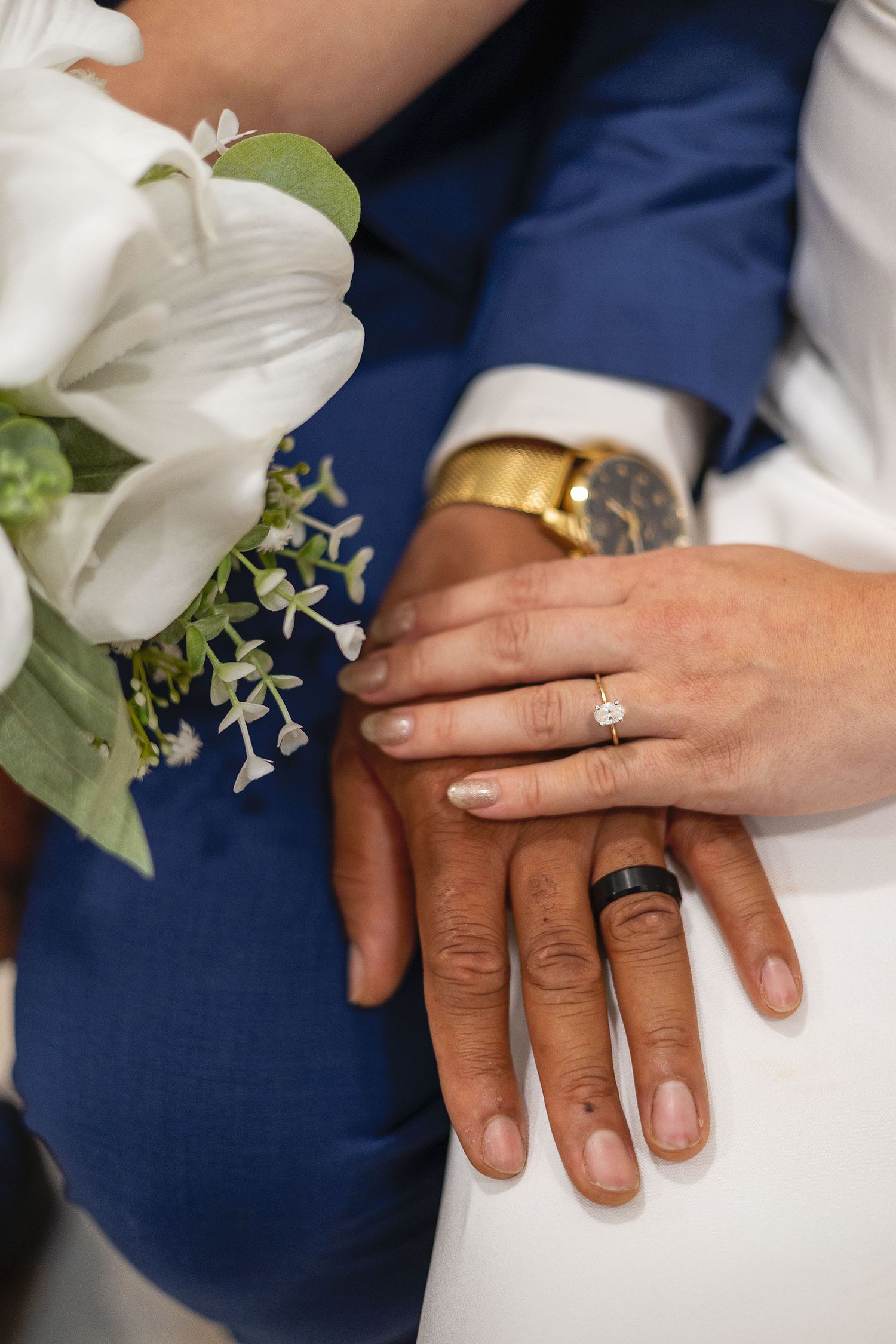 Newlyweds display their wedding rings, bride holding white calla lily bouquet, groom wearing gold watch.