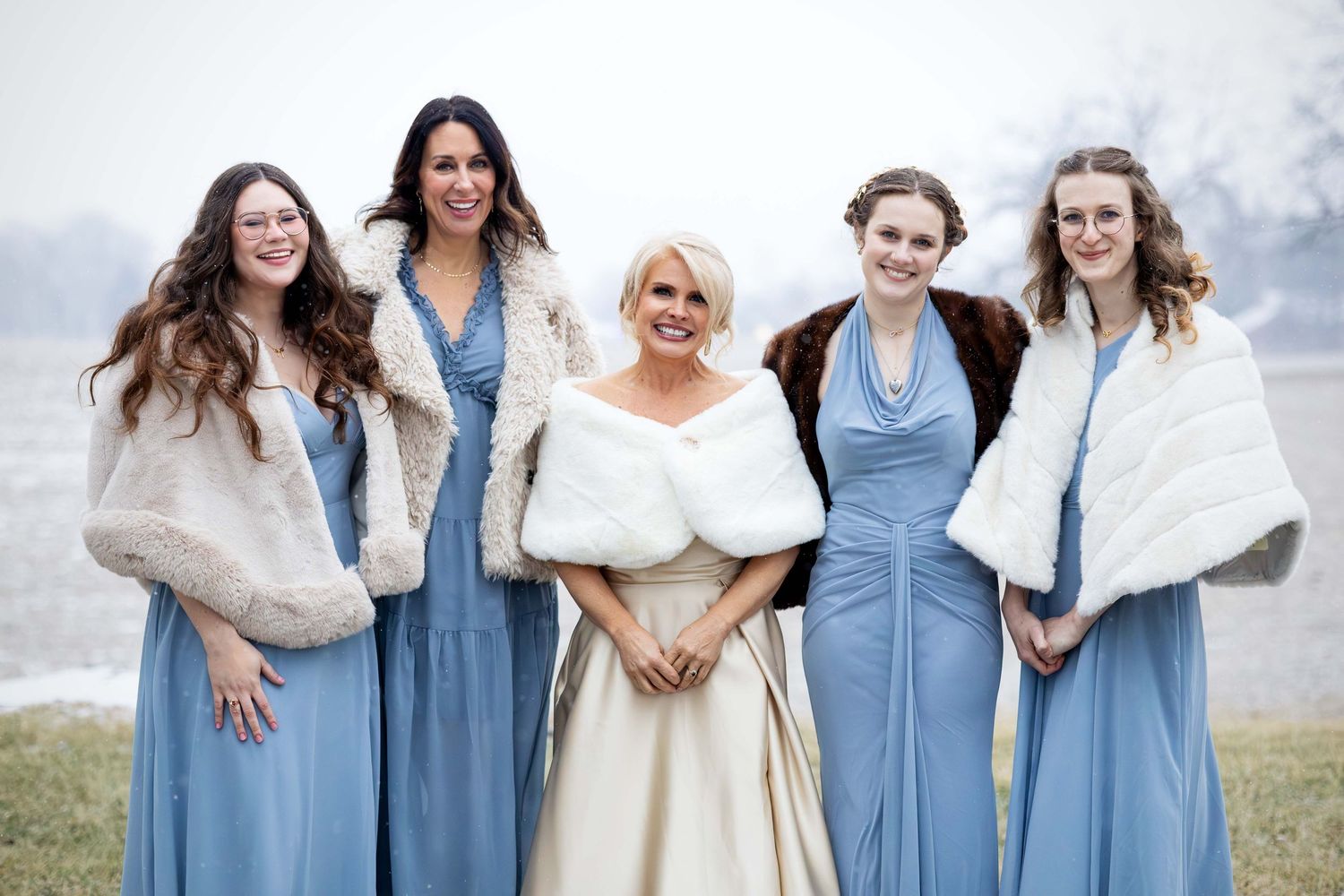 A bride in white fur wrap poses with four bridesmaids in blue dresses and fur stoles.