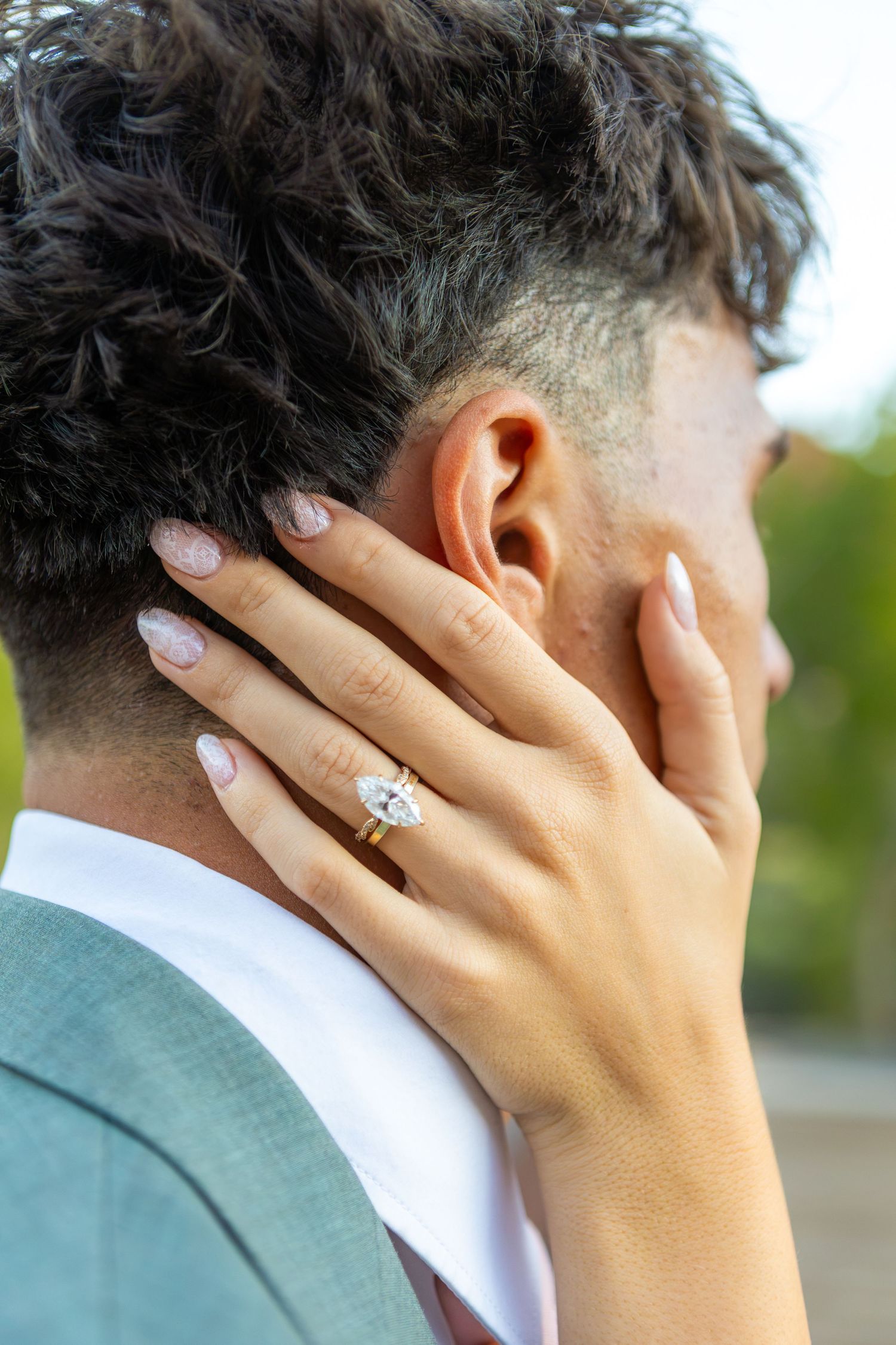 Close-up of a woman's hand with a diamond engagement ring resting on a man's neck.