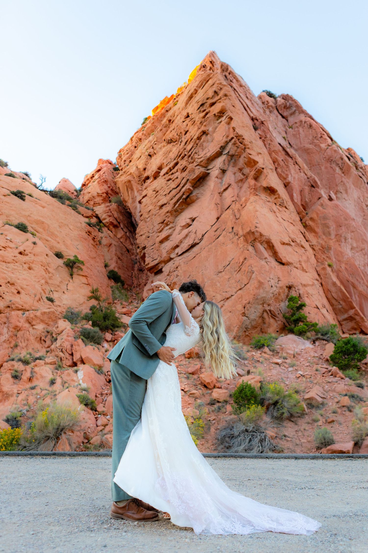 Bride and groom share a romantic kiss in front of stunning red rock formations during their outdoor desert wedding ceremony.