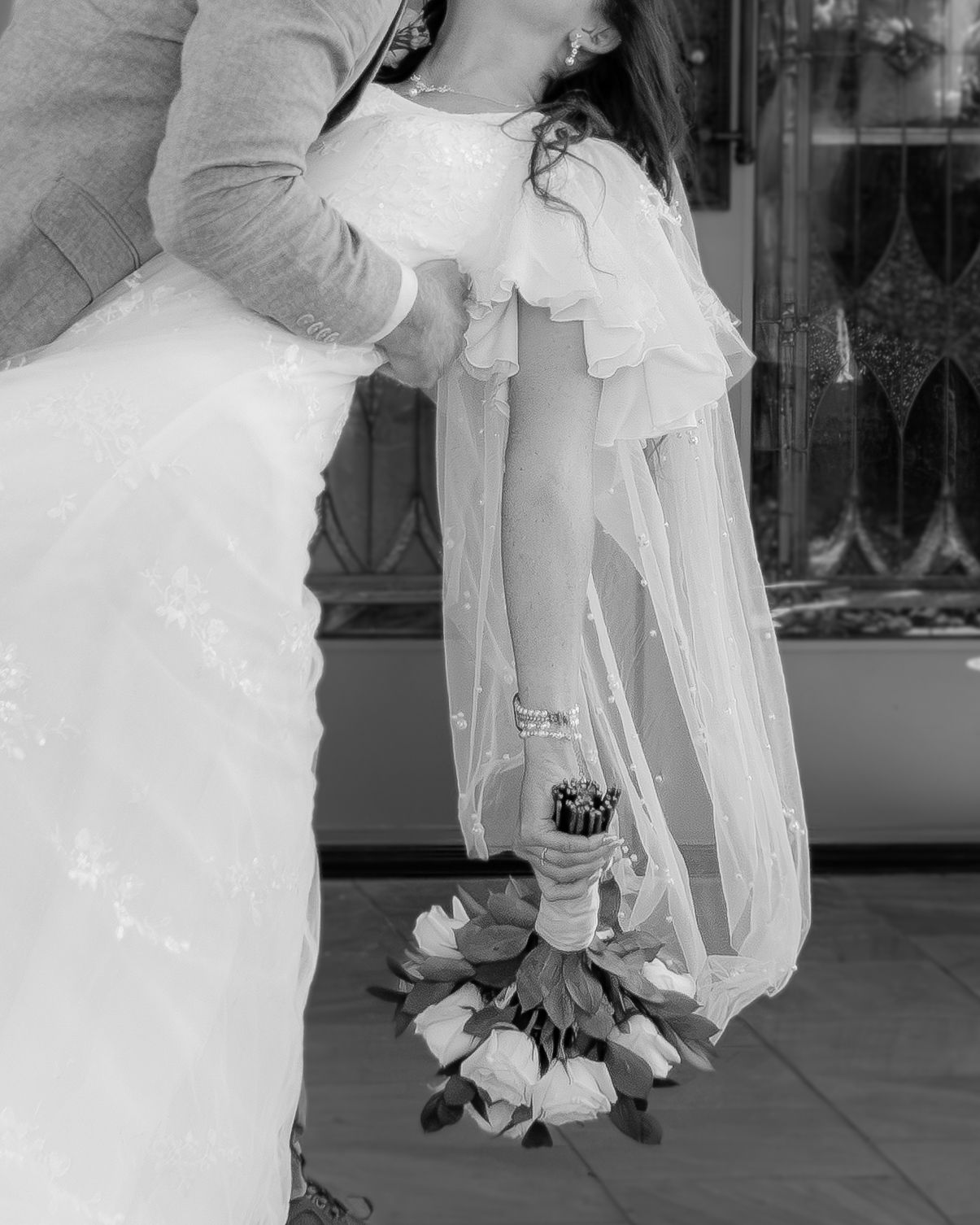 Black and white photo of a bride in a white gown holding a rose bouquet, embraced by a groom in a gray suit at the LDS Temple