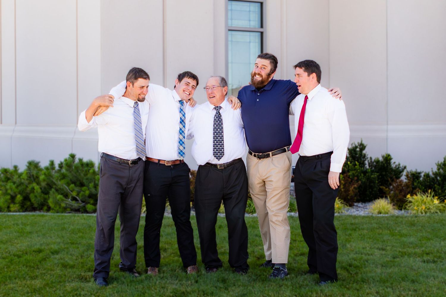 Five men in dress shirts and ties smiling and laughing together outdoors on green grass at Cedar City Utah Temple.
