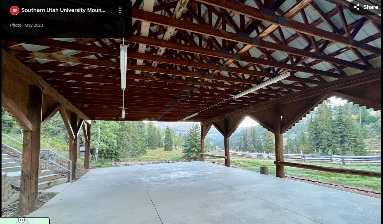 Covered outdoor pavilion with wooden beams and columns at Southern Utah University Mountain Center surrounded by pine trees.