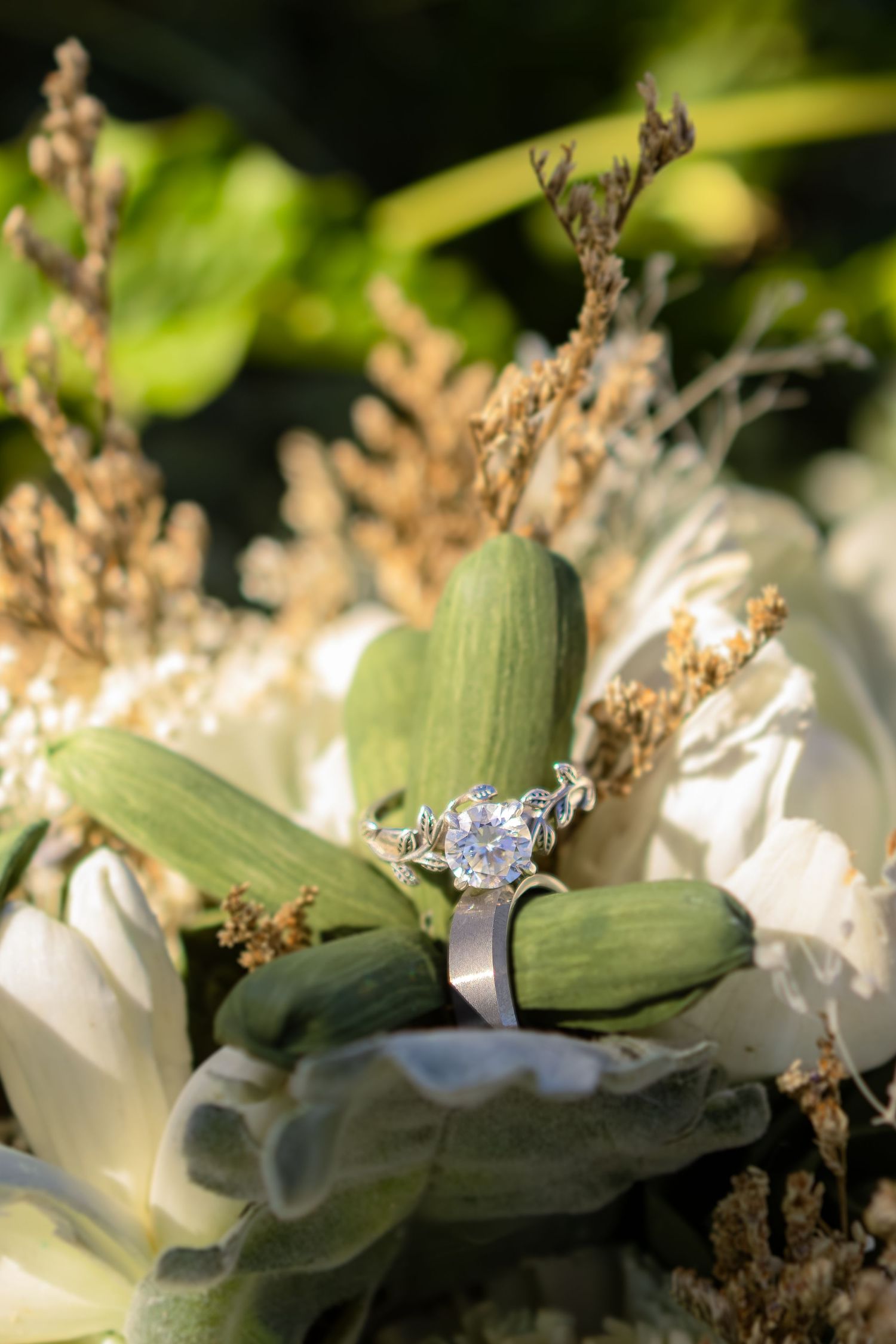 Silver diamond engagement ring resting on a bridal bouquet with white flowers and green stems.