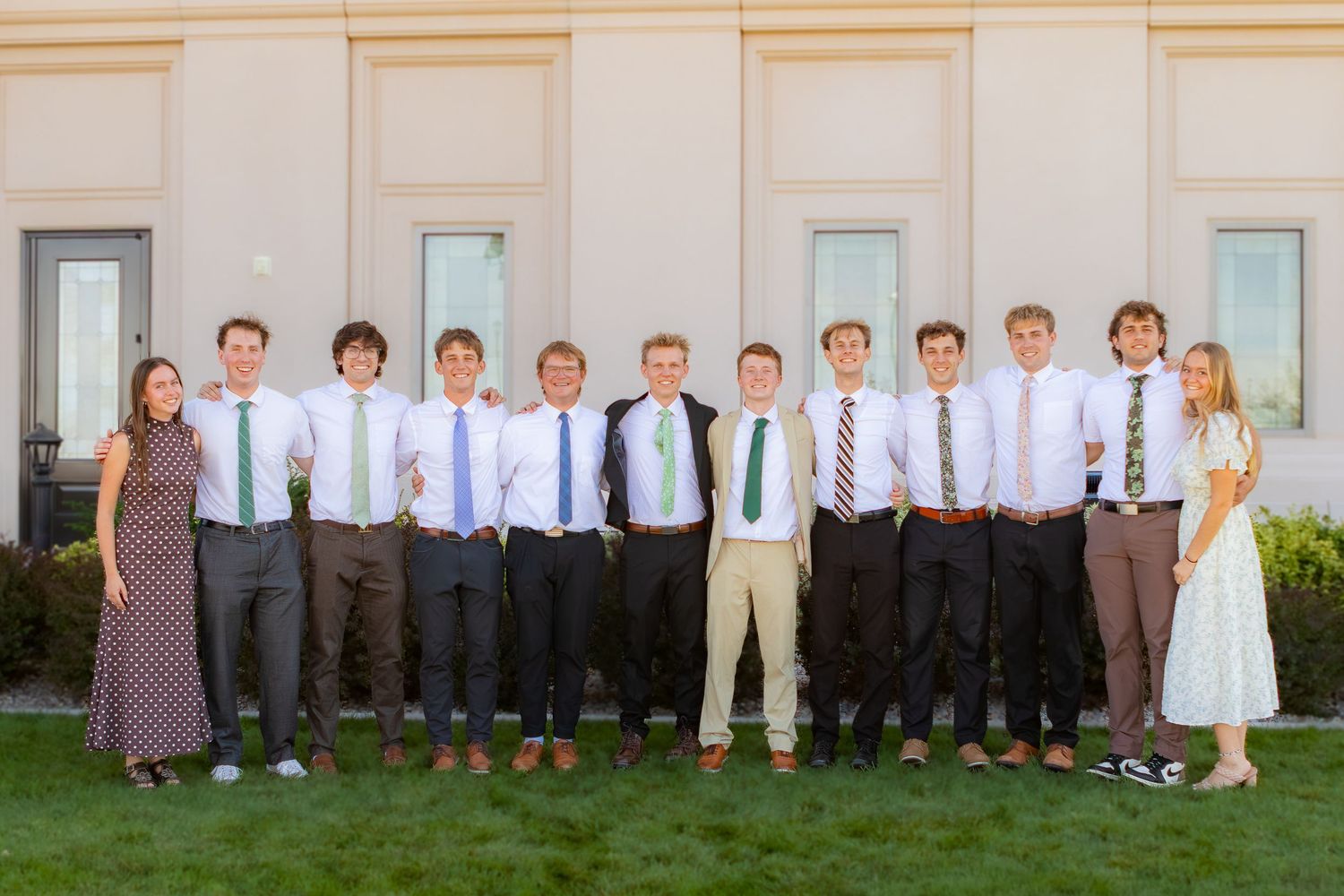 Group of young men in dress shirts and ties posing outdoors with two women on either side.